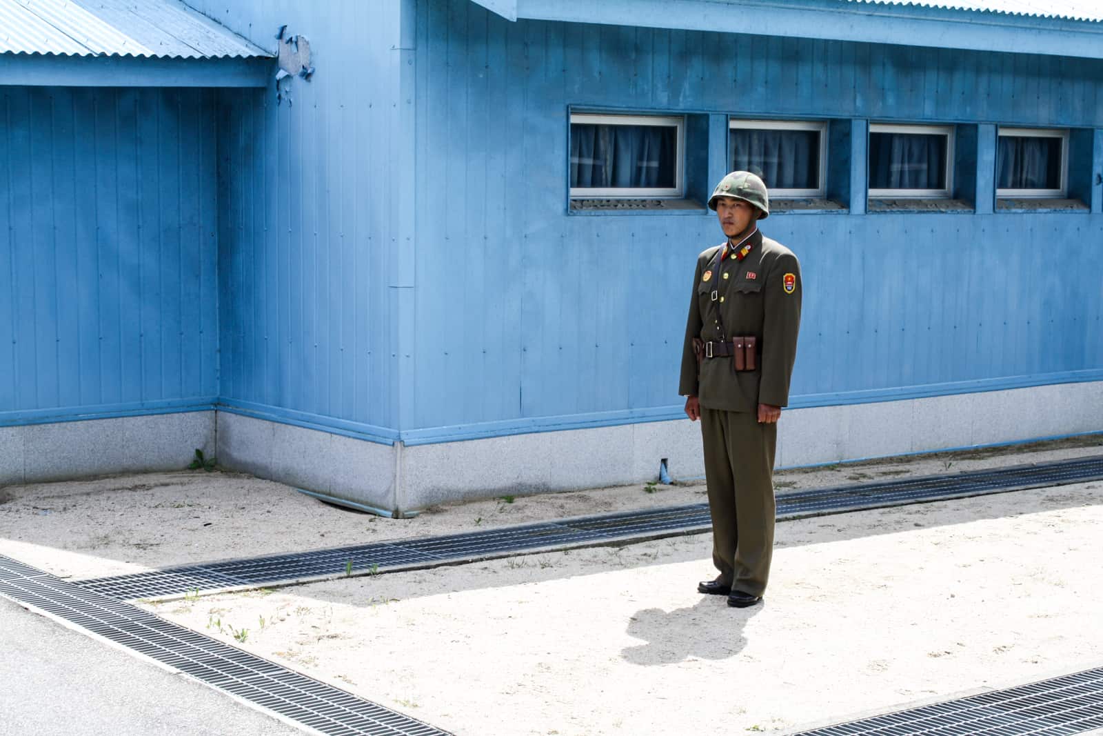 A North Korean guard dressed in an army green military uniform stands outside a blue hut at the DMZ on the North Korean side. 