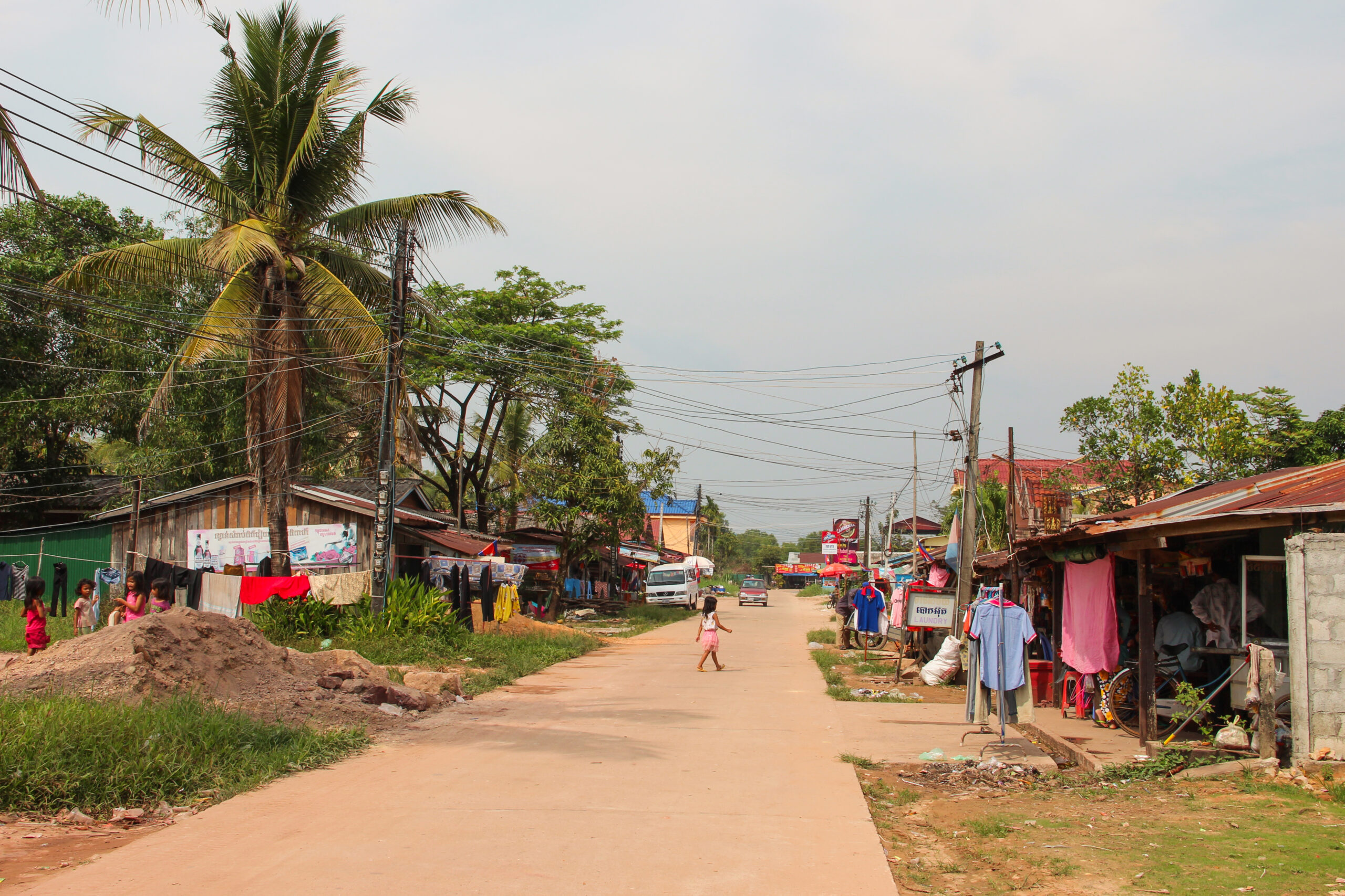 A small tree-lined streets with small houses covered in laundry, drying outside.