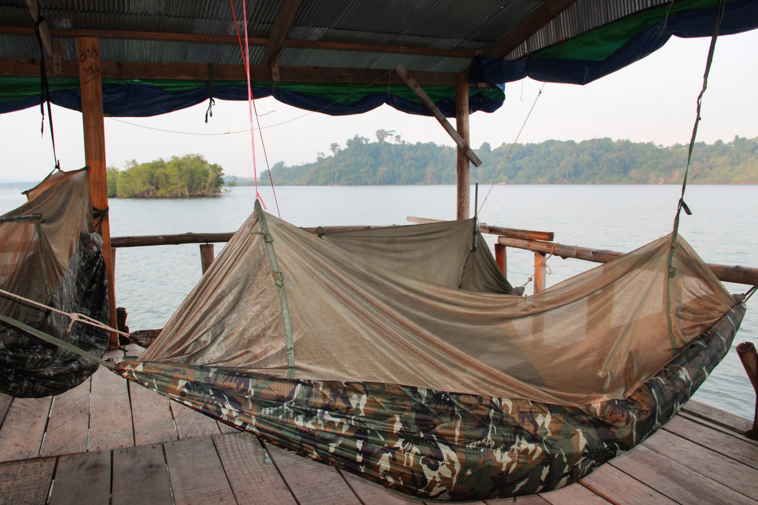 Army camouflage hammocks on a riverside wooden deck looking towards pockets of jungle and mangroves.
