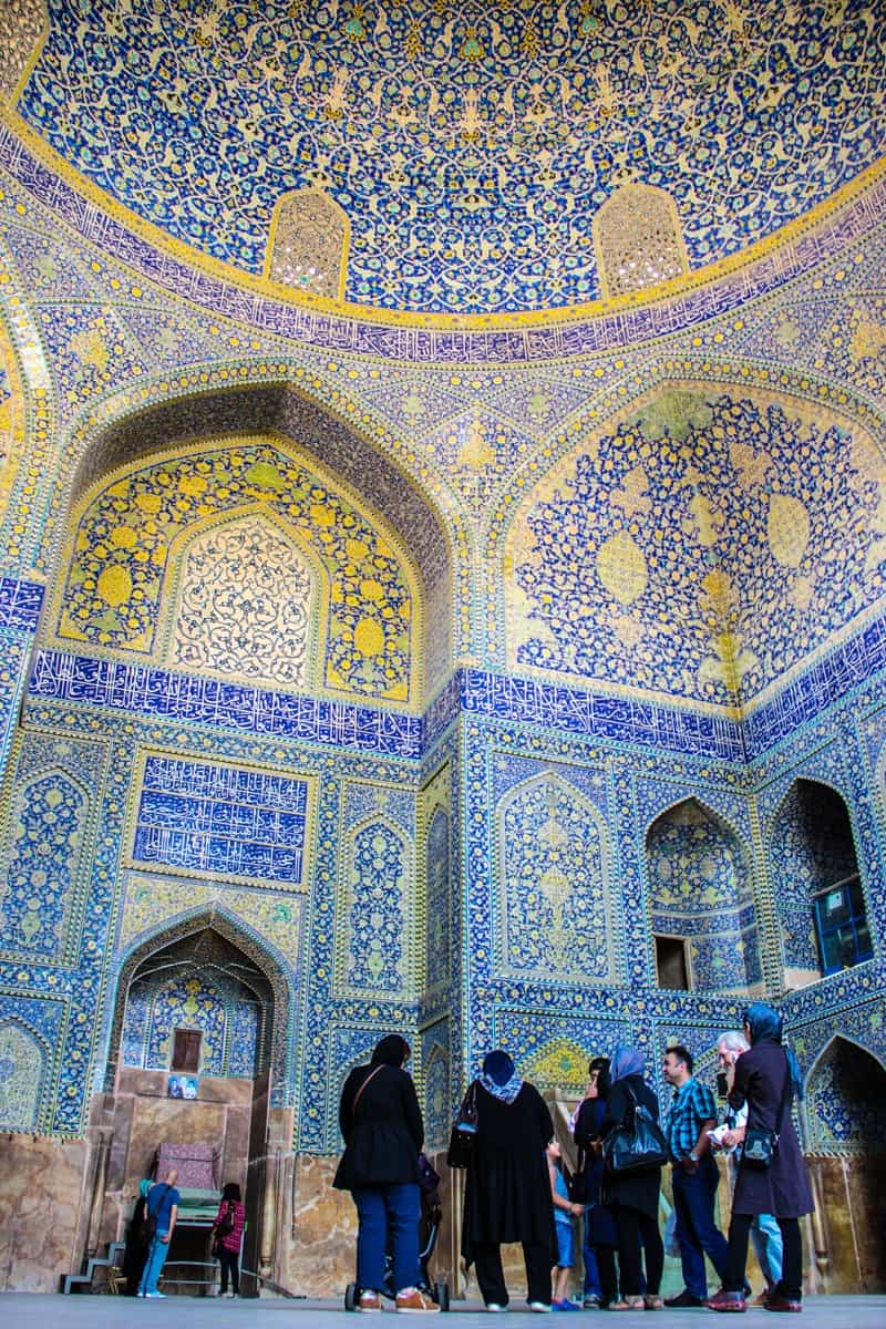 Tourists in Iran stand within the gold and blue mosaic interior of the Sheikh Lotfollah Mosque in Isfahan. 