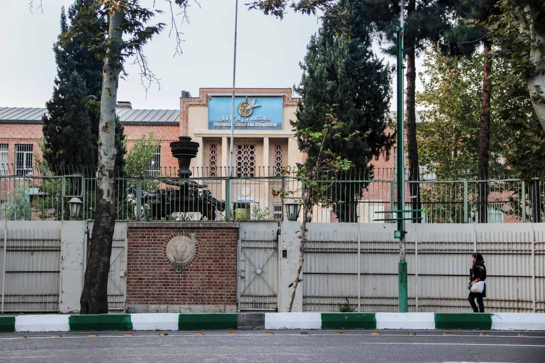A woman in black clothing walks past the high green gate in front of the former US Embassy in Tehran, Iran.