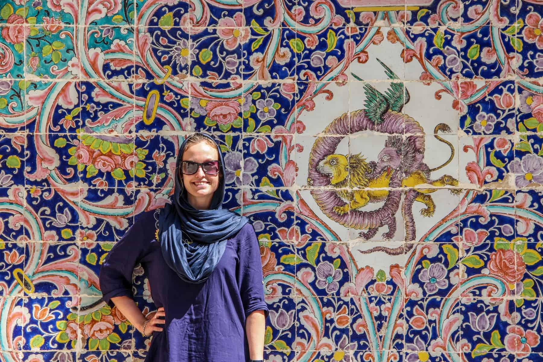 A female tourist in iran dressed in long-sleeved clothing and a headscarf, standing in front of the pretty mosaic tiles of Golestan Palace in Tehran. 