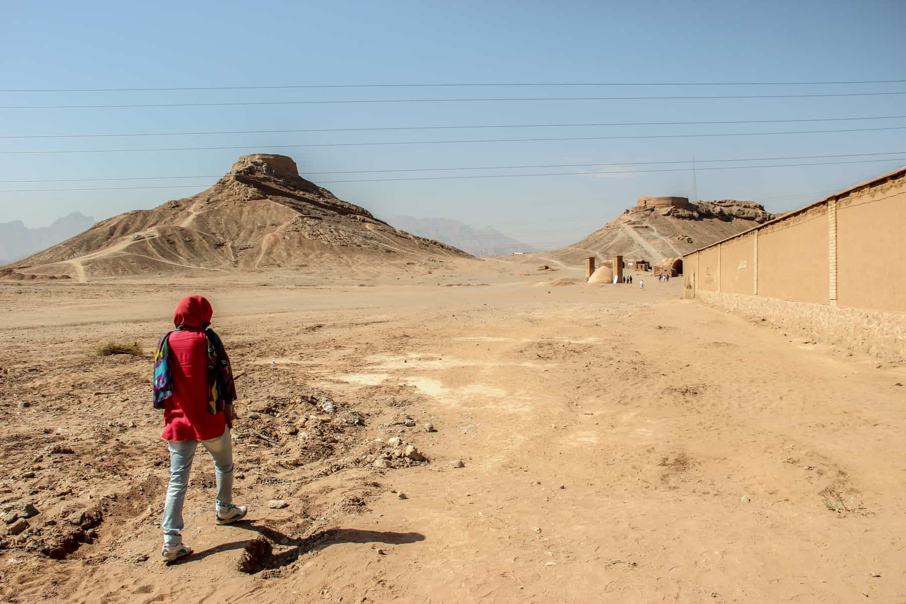 A woman in red walking through the desert towards the Zoroastrian Towers of Silence in Yadz, Iran. 