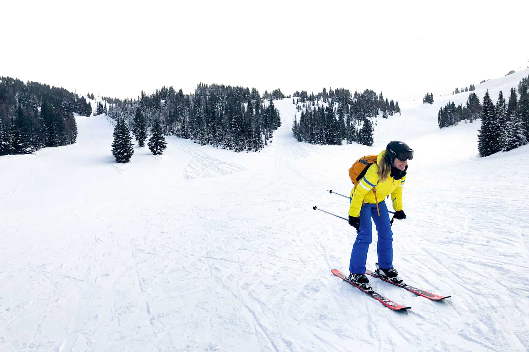 A woman in a yellow and blue ski outfit going downhill on a snow slope.