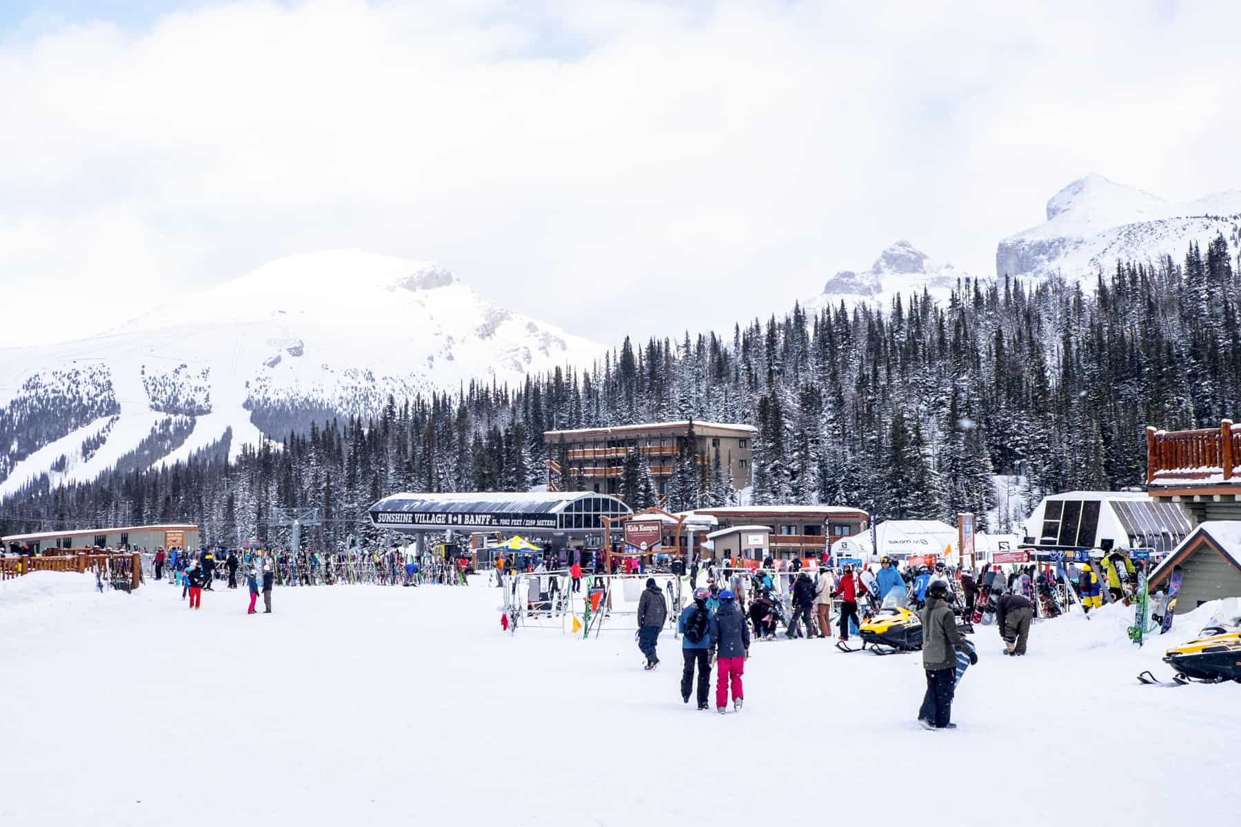 People gather at the highest ski slope on Sunshine Village Resort in Banff full of wooden buildings. 