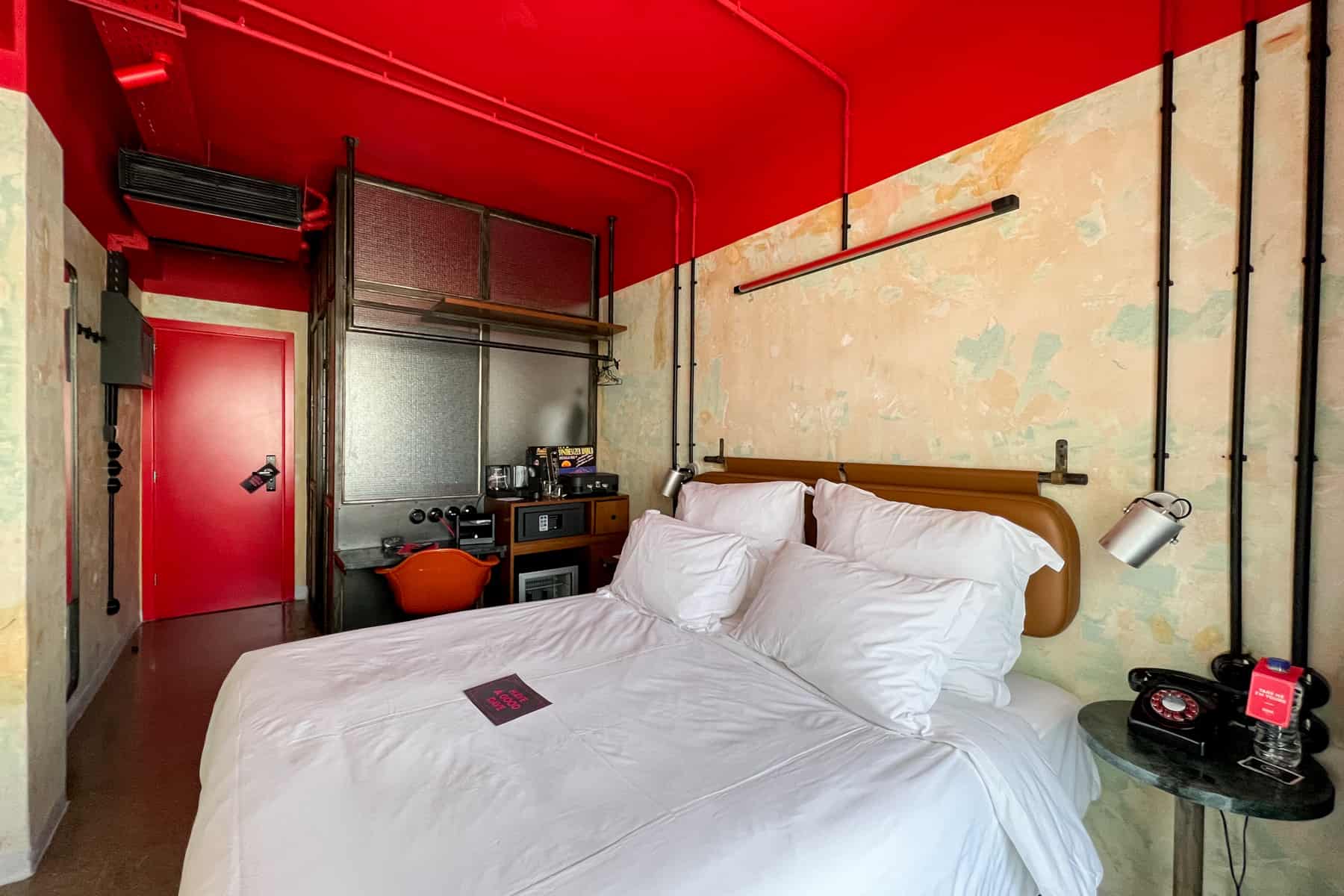 A white bed in an urban hotel room with a red ceiling and retro trims. 