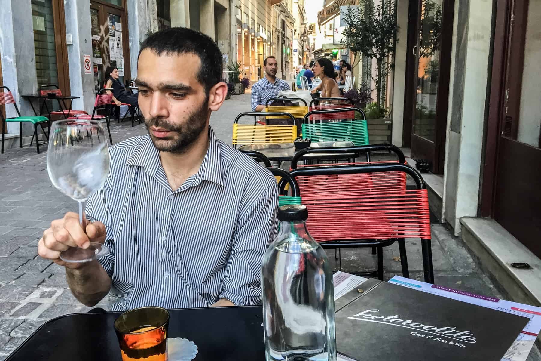 A man looks at a wine glass while sitting outside of the Heteroclito wine bar in Athens. 