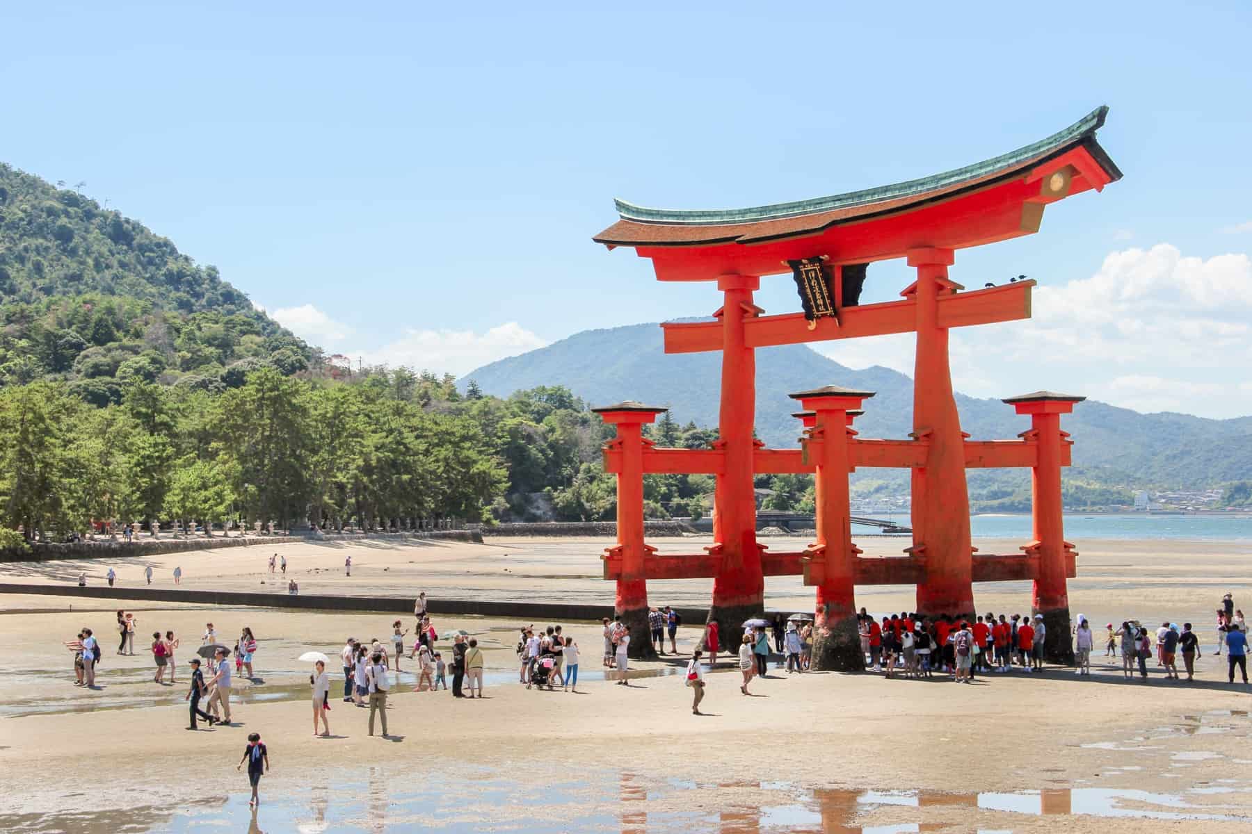 A red Japanese tori gate on a forest backed beach - the Itsukushima Floating Torii Gate on Miyajima Island..
