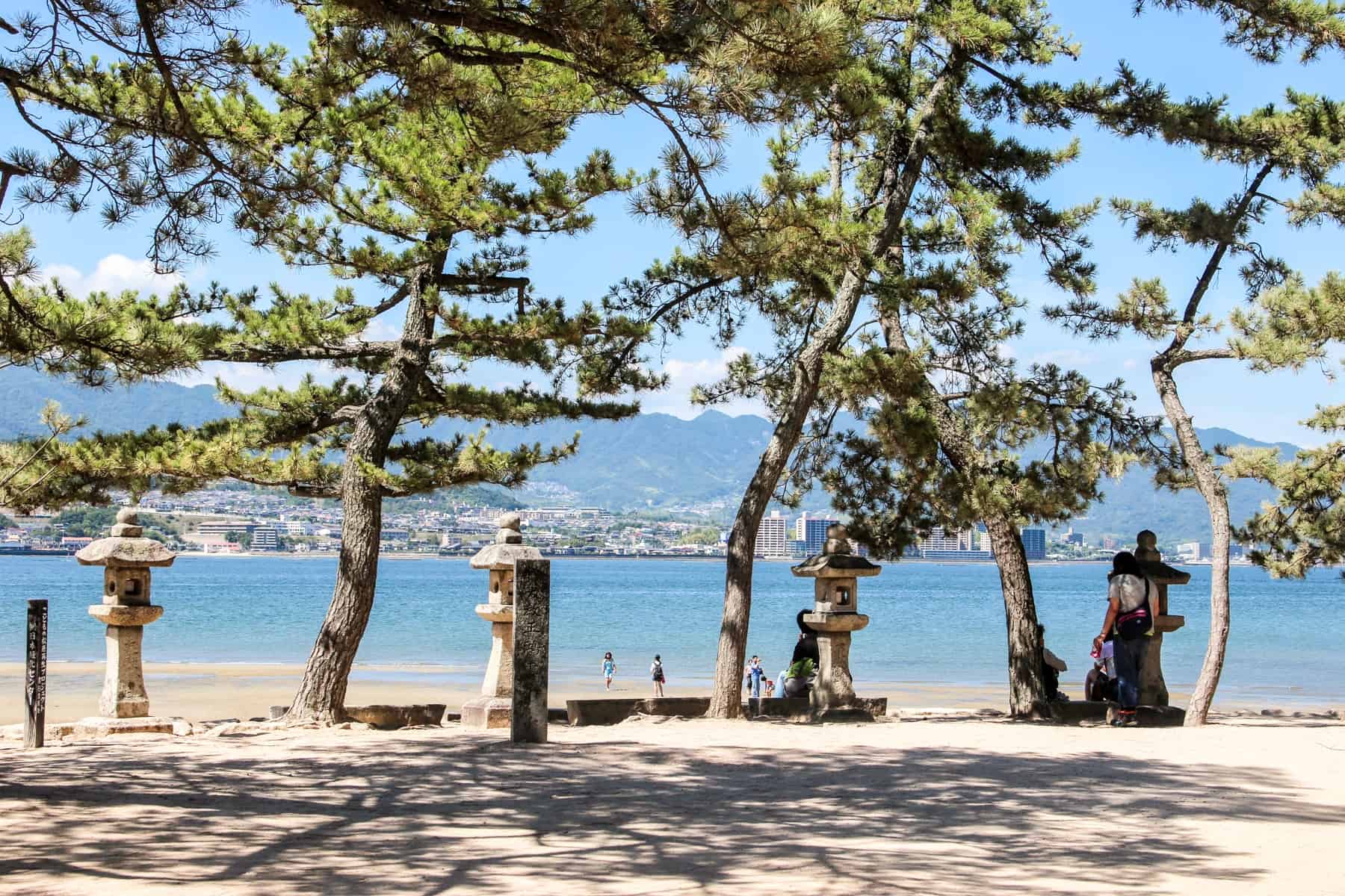  Itsukushima Island's tree lined coastline with small tiered pillars looking towards the mainland of Japan. 