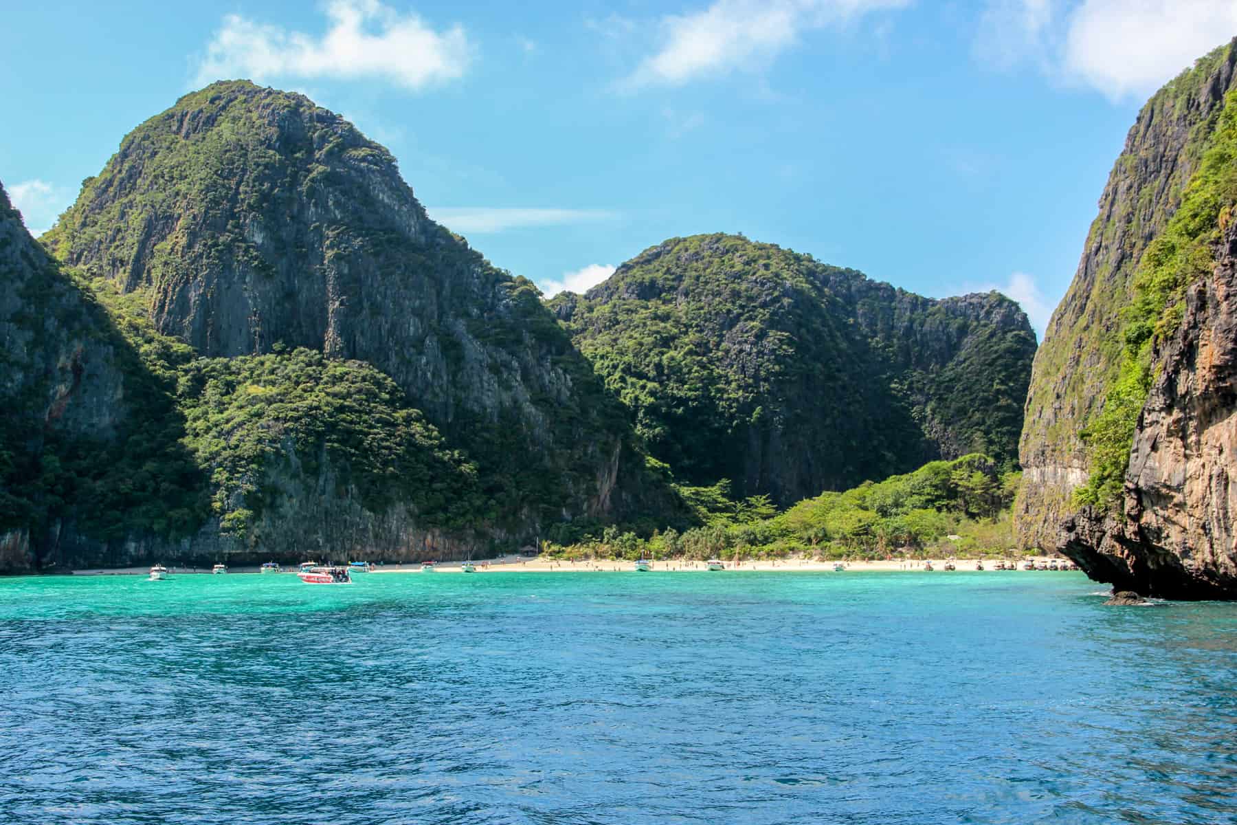 The grassy cliff-backed, bright yellow sand and bright blue water cove of the famous Maya Bay in Thailand. 