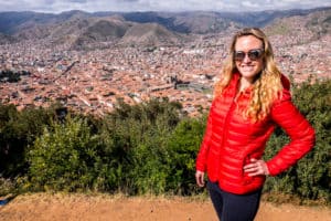A woman in a red coat standing at a elevated point overlooking the vast valley of Cusco, Peru.