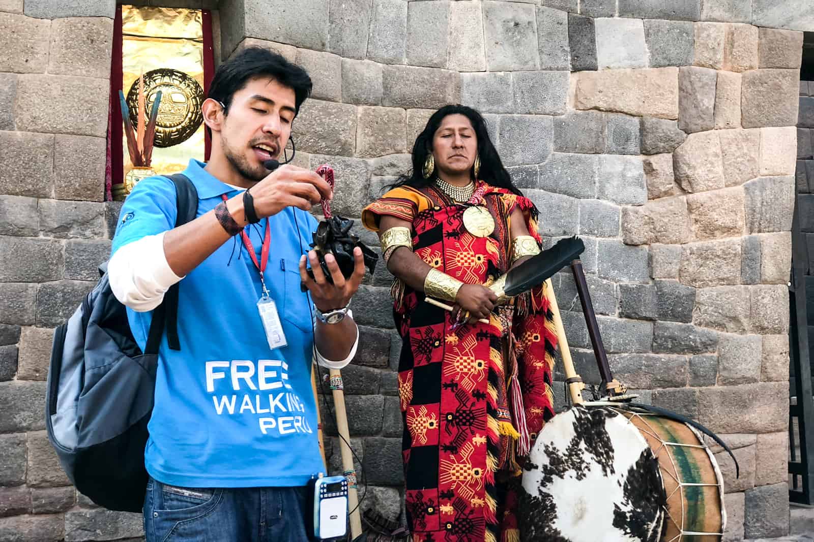 A Free Walking Tours Peru guide in a blue t-shirt with a Peruvian man in traditional dress holding a drum. 