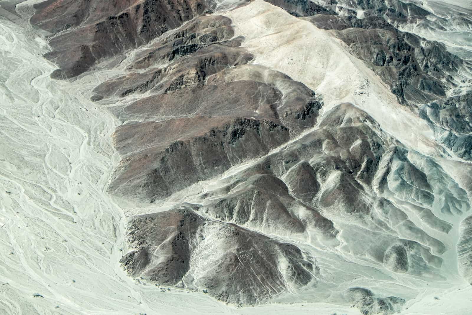 A brown rocky desert landscape with an astronaut carving on the bottom rock - one of the Nazca Lines you can fly over and see on a Peru trip. 