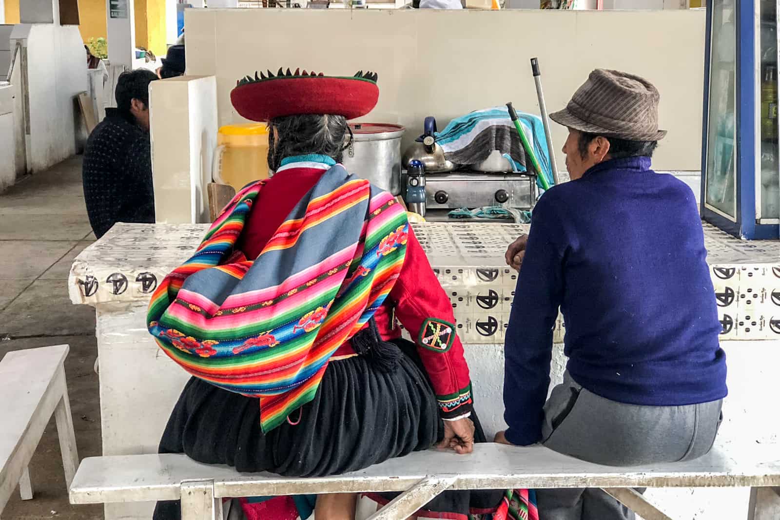 A Peruvian couple (the woman in traditional woven clothing and a red hat) eating in a market in Cusco, Peru.