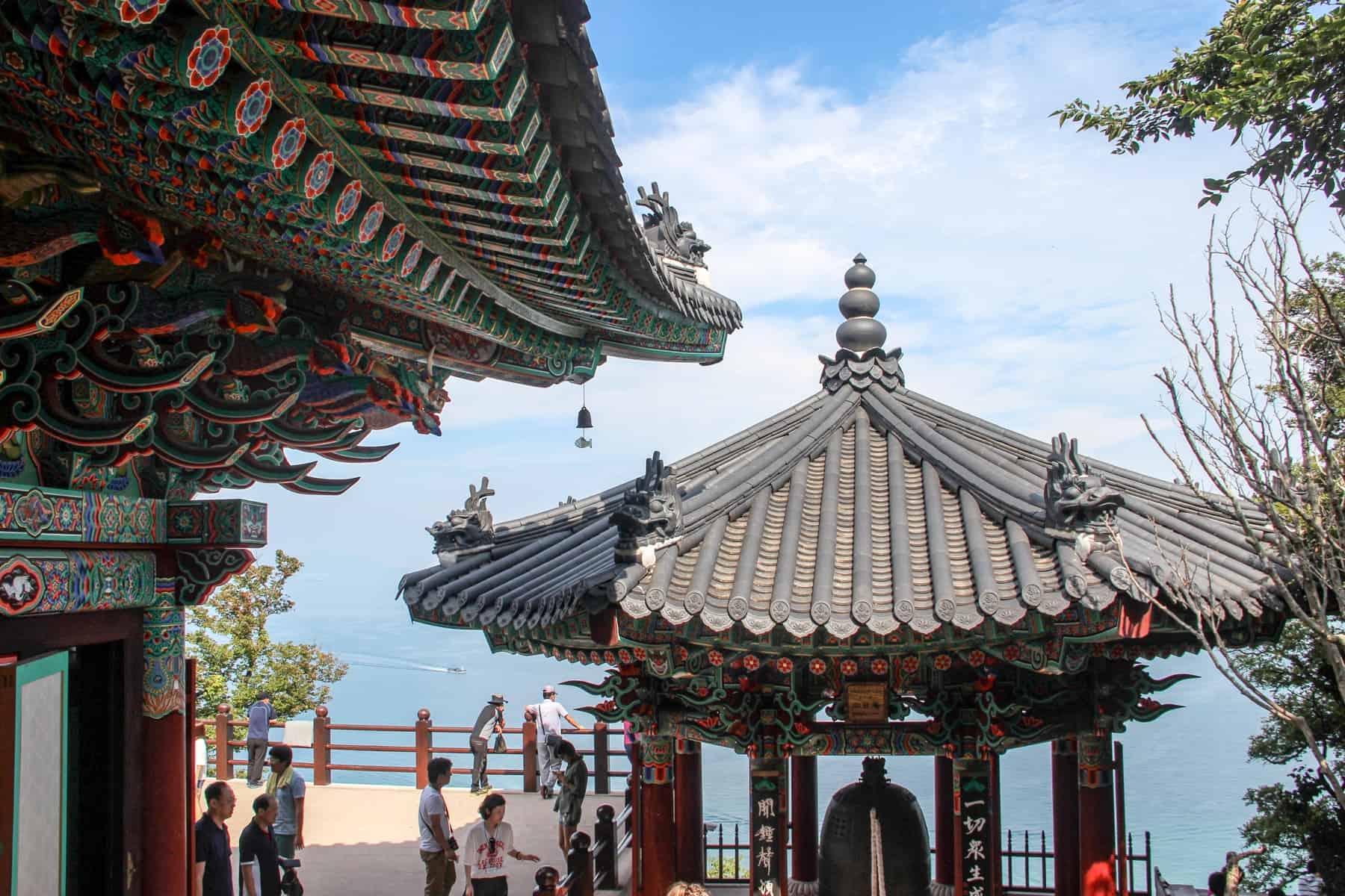 The colourful painted wood roof of Geomosan Hyangilam temple in Yeosu, with a view overlooking the ocean. 