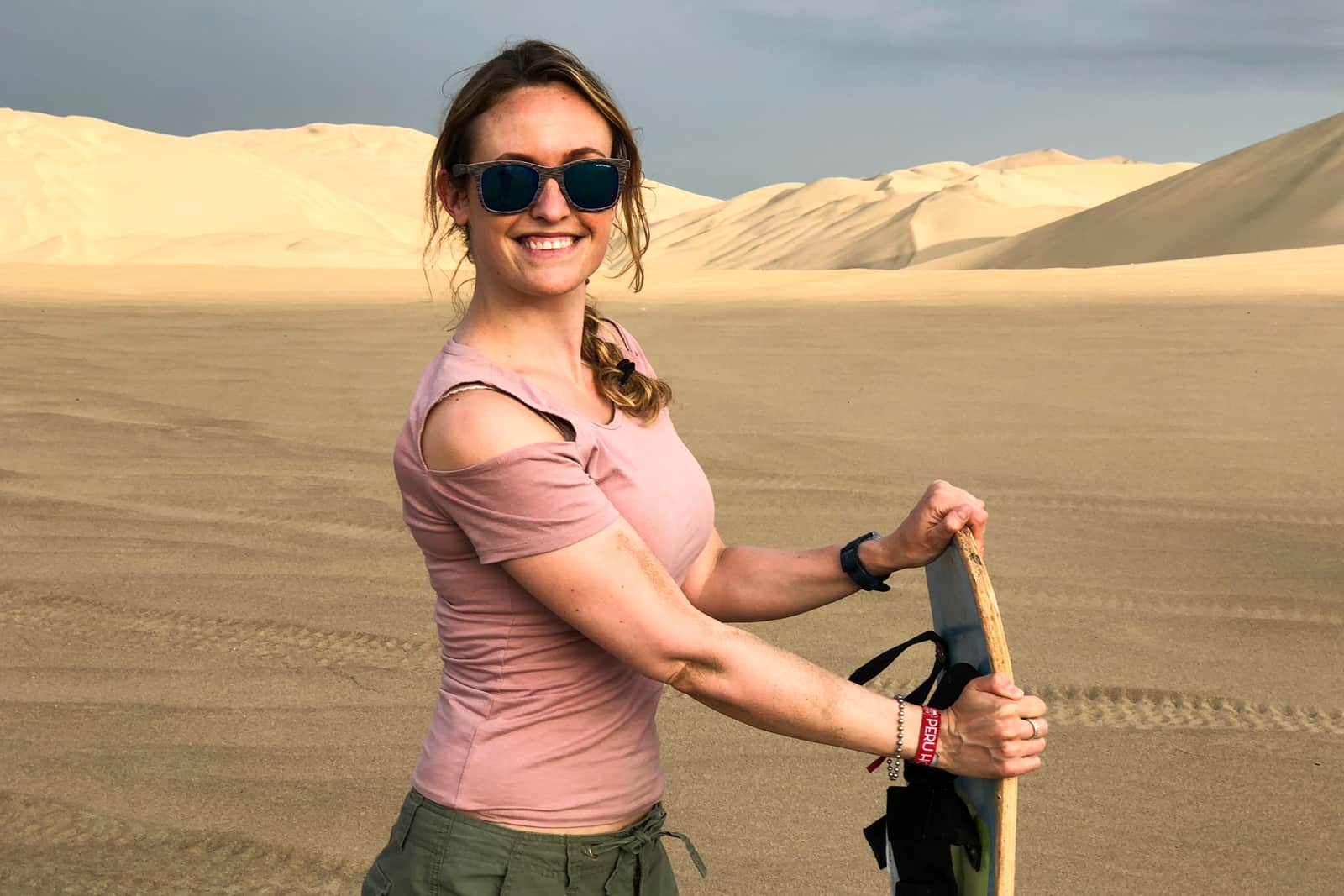 A woman holding a sandboard while in the Huacachina sand dunes in Peru. 