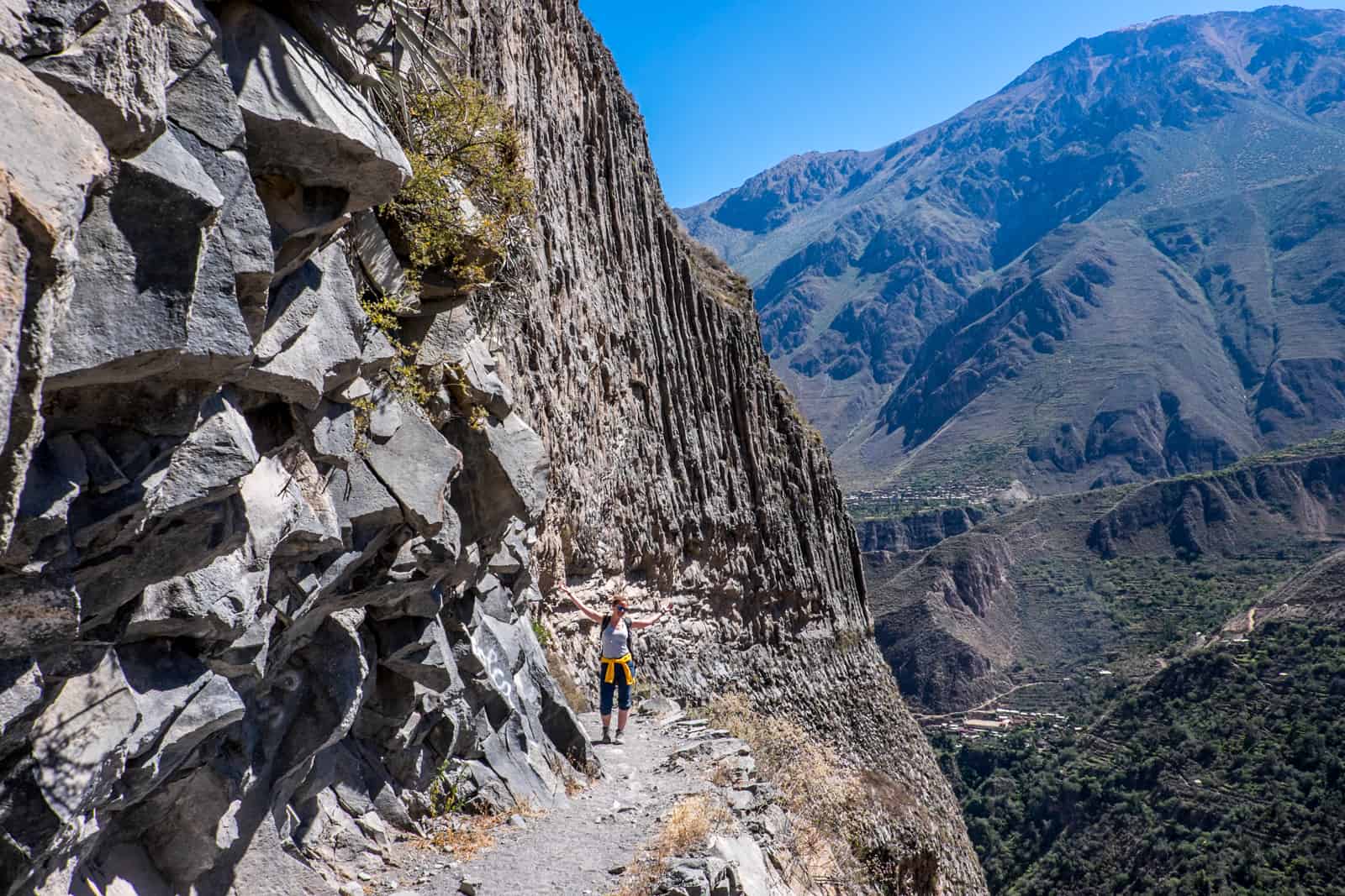 A tourist on a rock ledge path trekking in Colca Canyon in Peru.