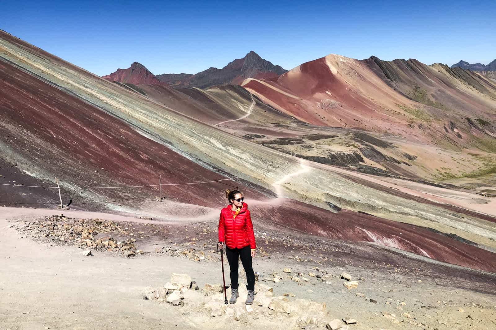 A woman stands in front of the multi-coloured peaks having completed the Rainbow Mountain trek in Peru. 