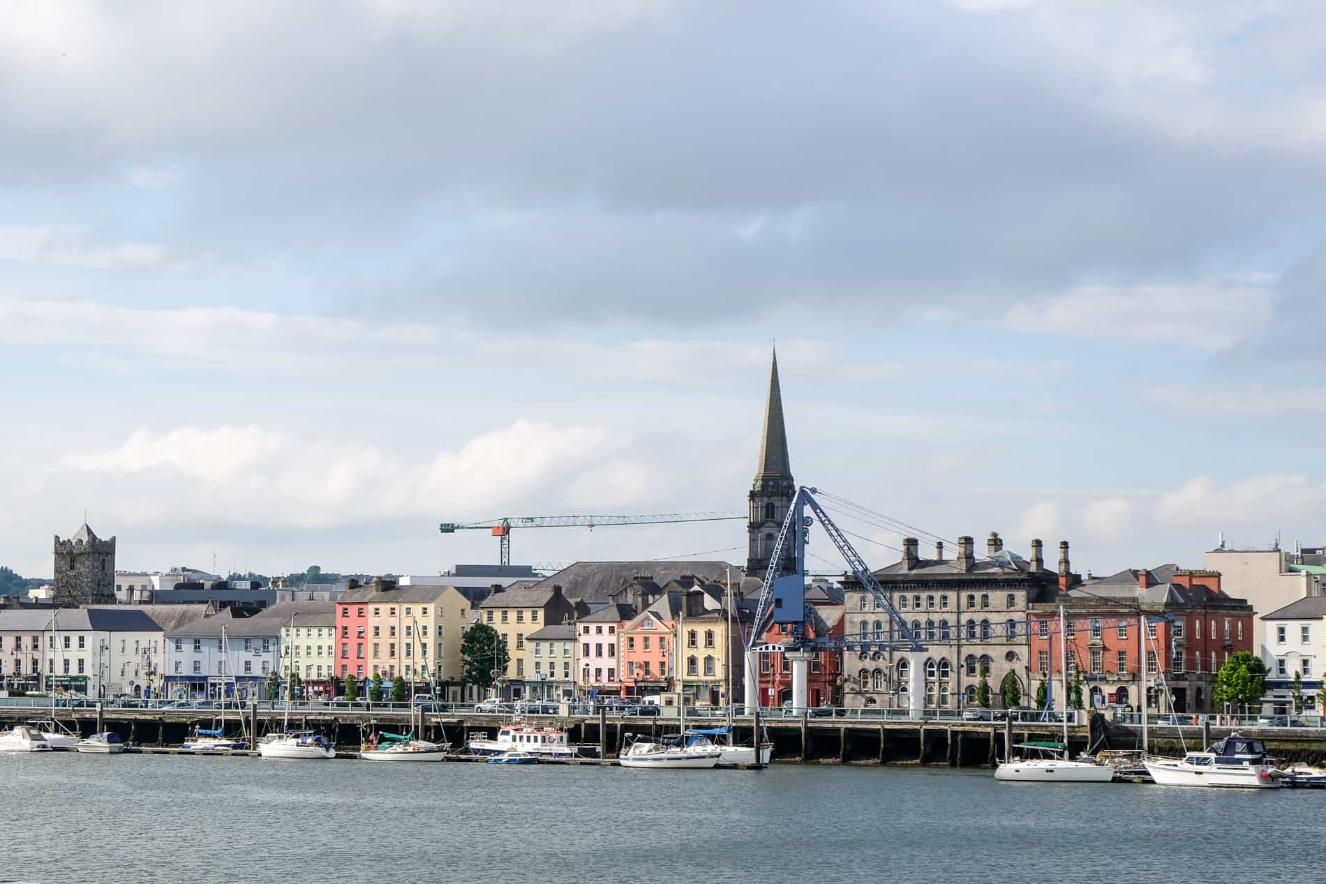 Famed view of Waterford, Ireland - a row of colourful houses on the riverside with medieval spires and towers poking through. 