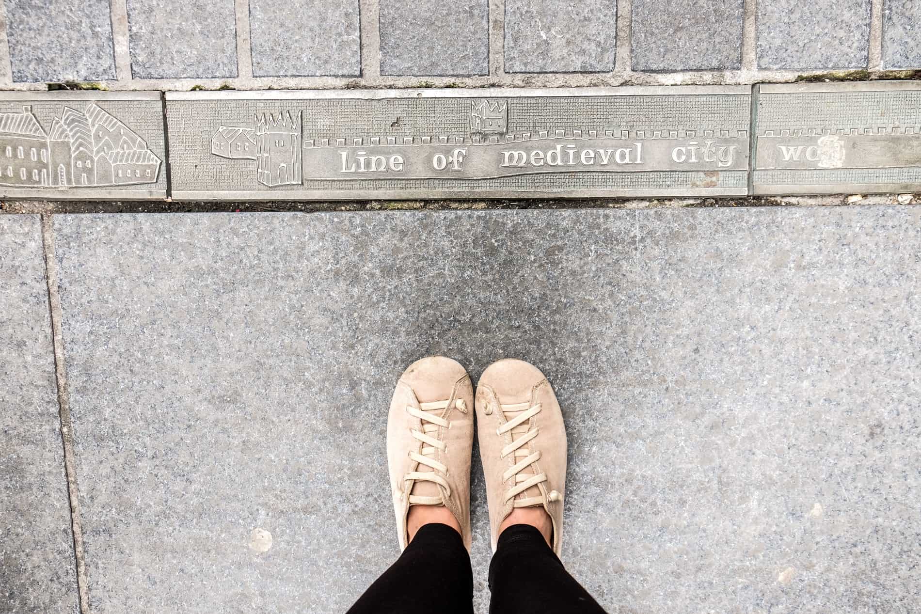 A carved metal marker on a pavement shows the Line of the Medieval City Wall of Waterford. 
