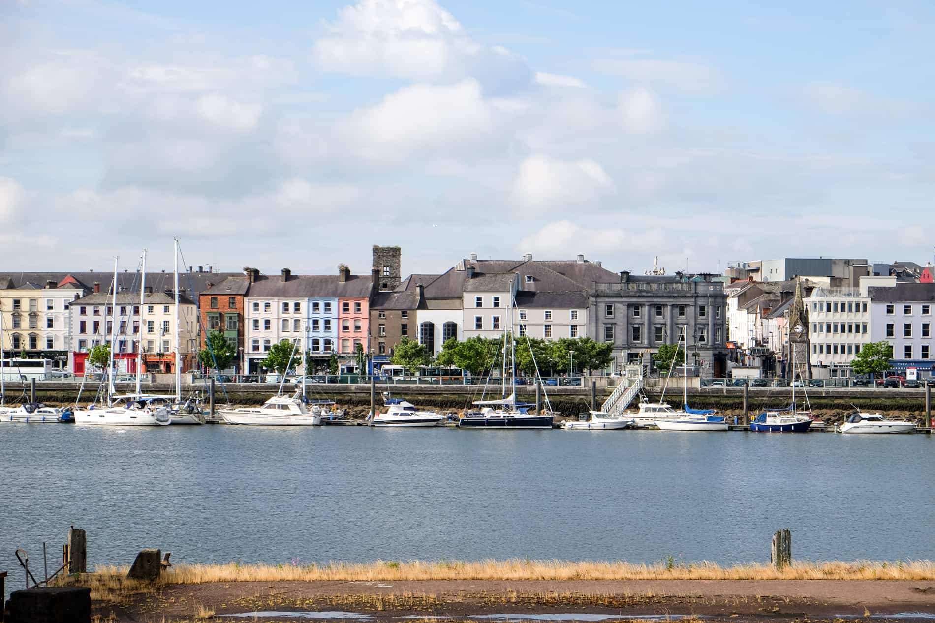 Famed view of Waterford Ireland - a row of colourful houses on the riverside with medieval spires and towers poking through.