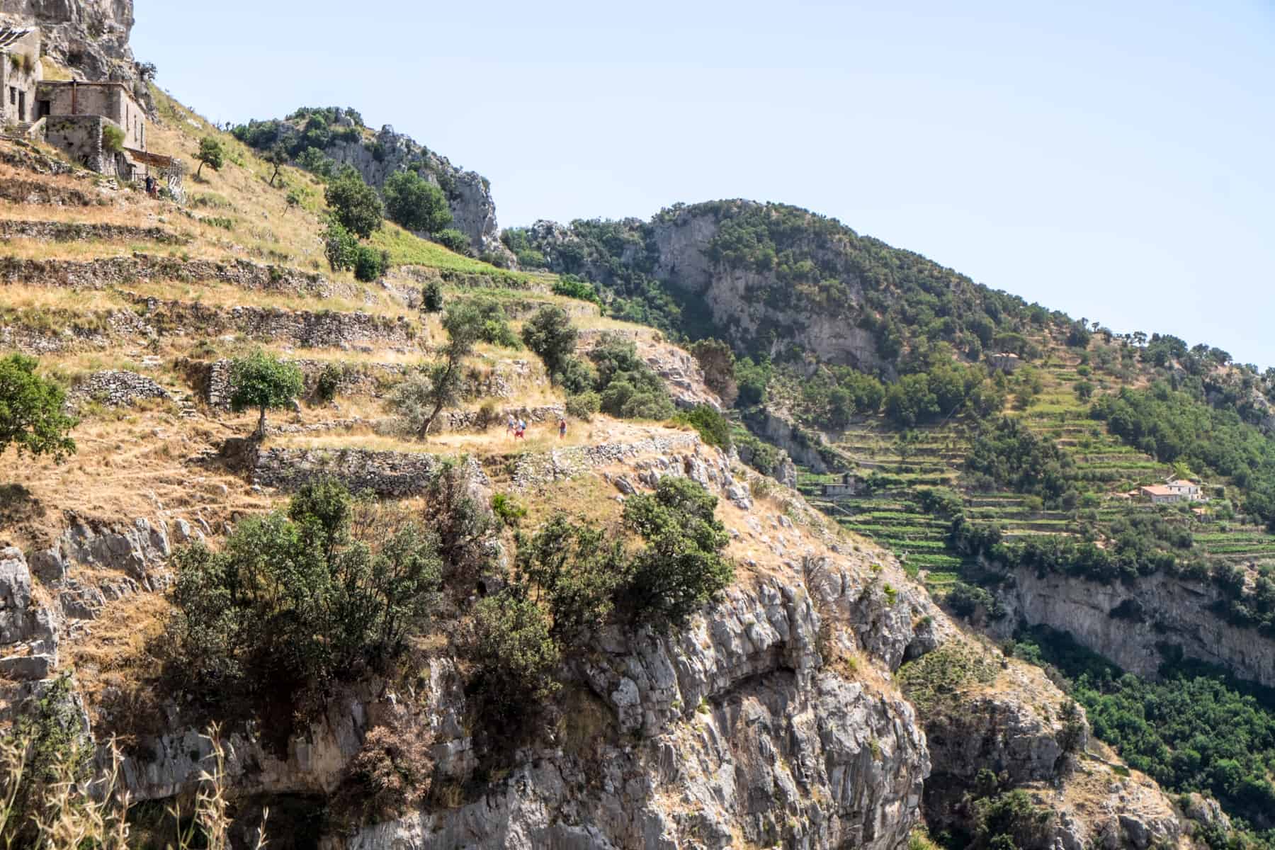 Hikers on yellow rock terrace trails on the Path of the Gods in the Amalfi Coast mountains. 