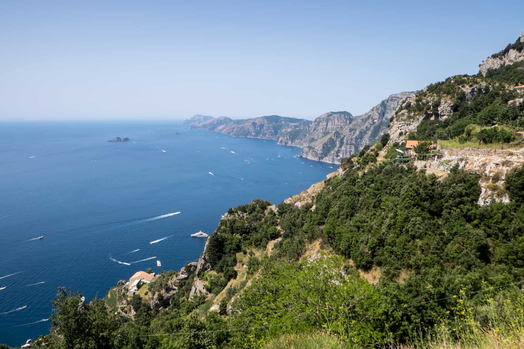 A high rocky pathway on a green clifftop overlooking the sea - part of the Path of the Gods hike in Amalfi, Italy.