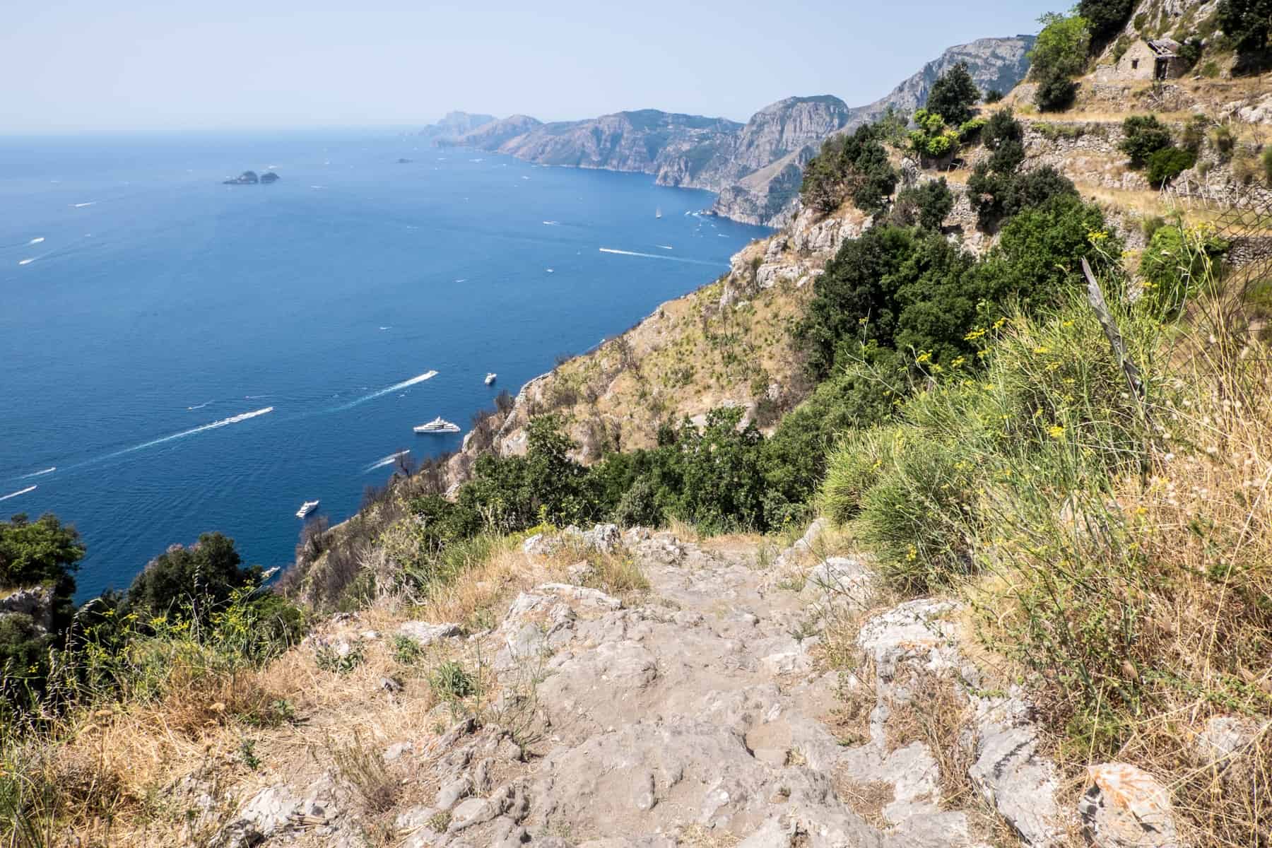 A high rocky pathway on a green clifftop overlooking the sea - part of the Path of the Gods hike in Amalfi, Italy. 