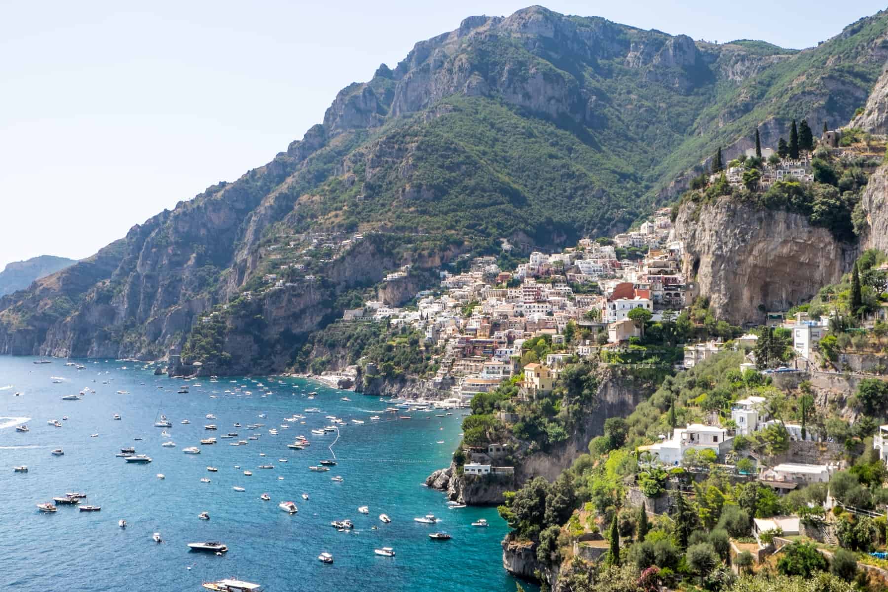 An elevated, distant view of the colourful cluster of houses of Positano town on the mountainous Amalfi Coast. 