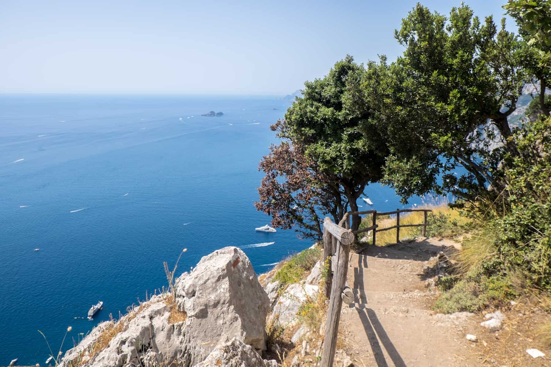 A downhill staircase through trees on the Path of the Gods, overlooking the deep blue sea on the Amalfi Coast.