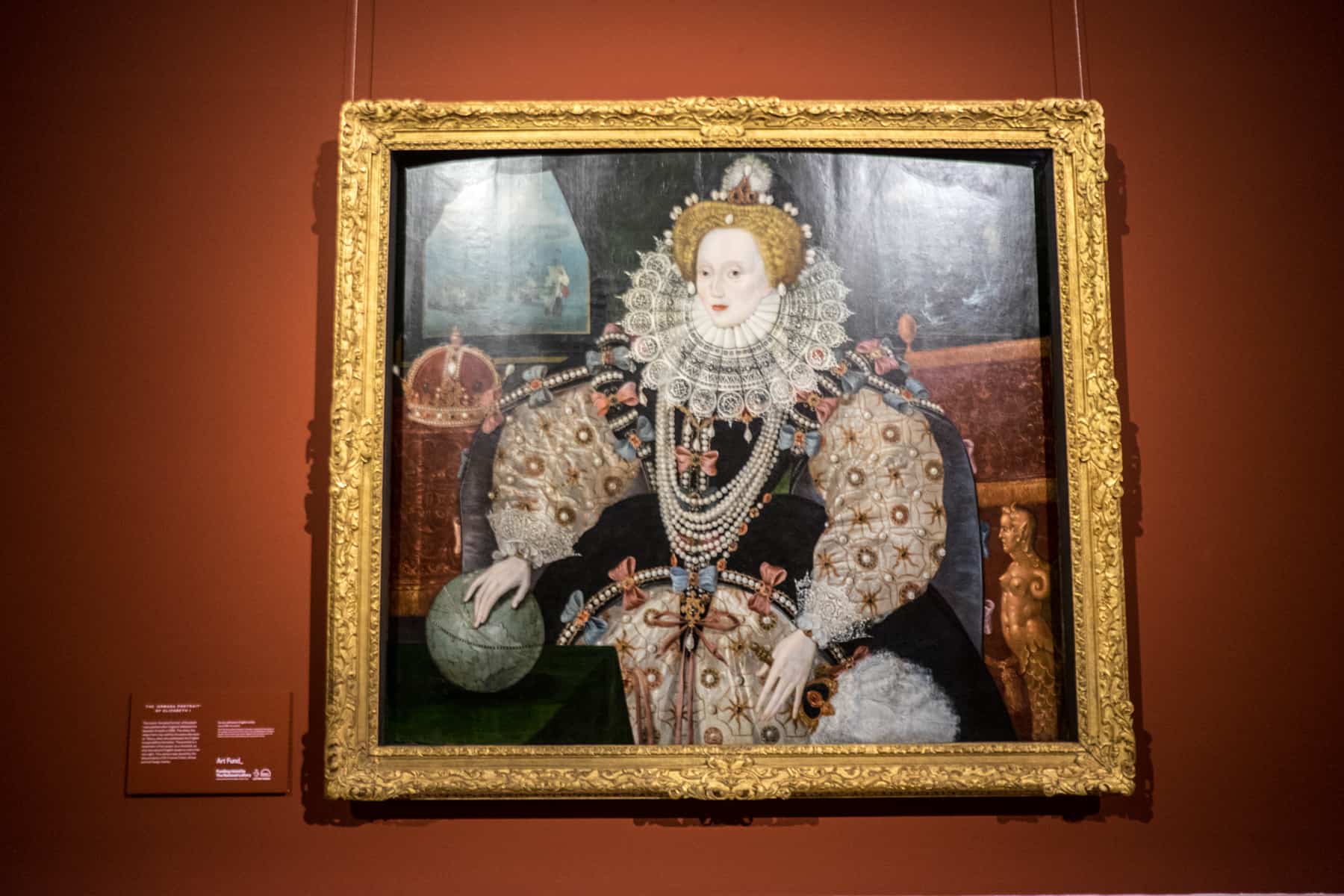 The famed ‘Armada Portrait’ of Elizabeth I on display with a gold frame on a red wall inside the Queen's House in Greenwich.