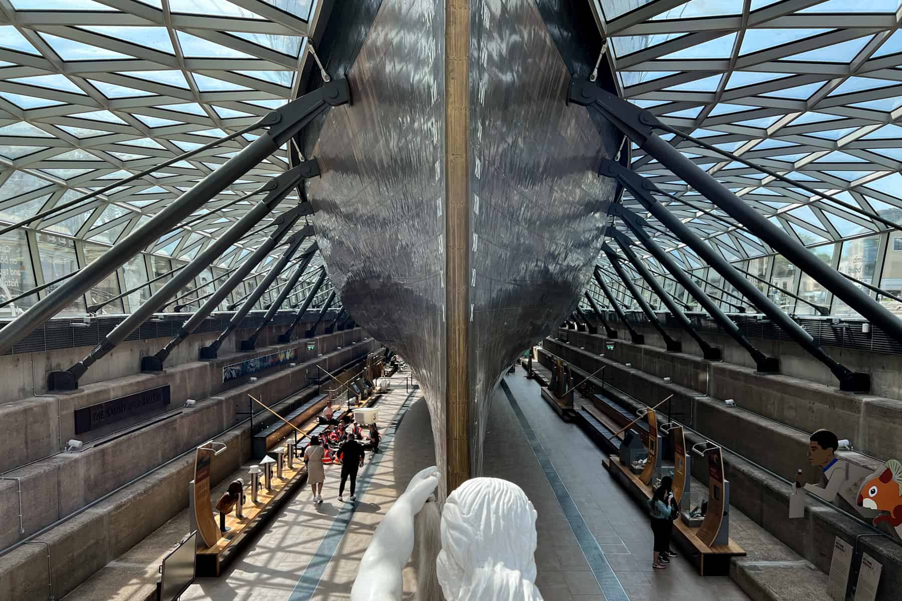 The Cutty Sark ship's gleaming copper hull underneath a glass roof and hoovering over museum space.