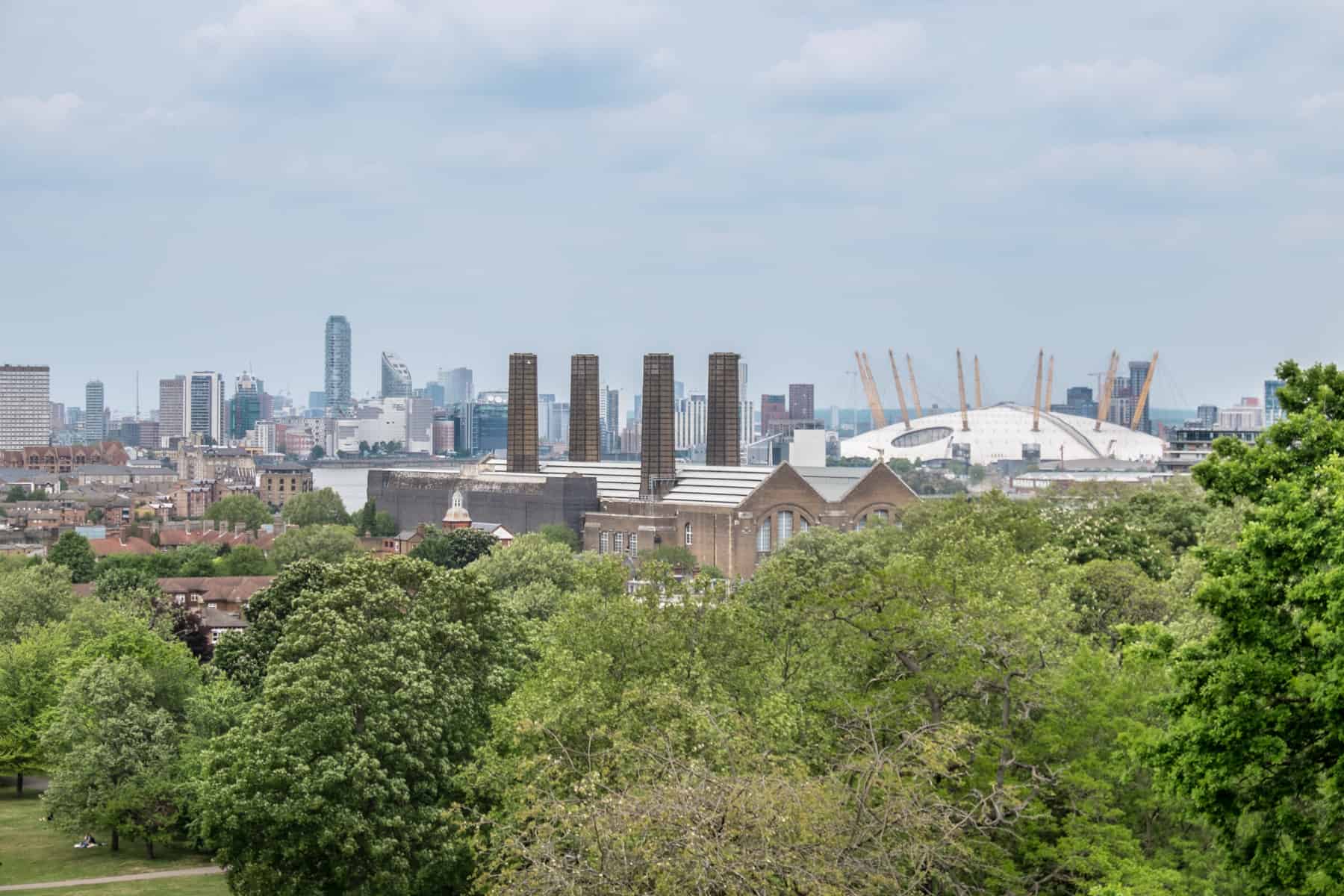 A view to the North Greenwich Peninsula and the white dome O2 Arena with yellow towers, behind an old chimney factory building.