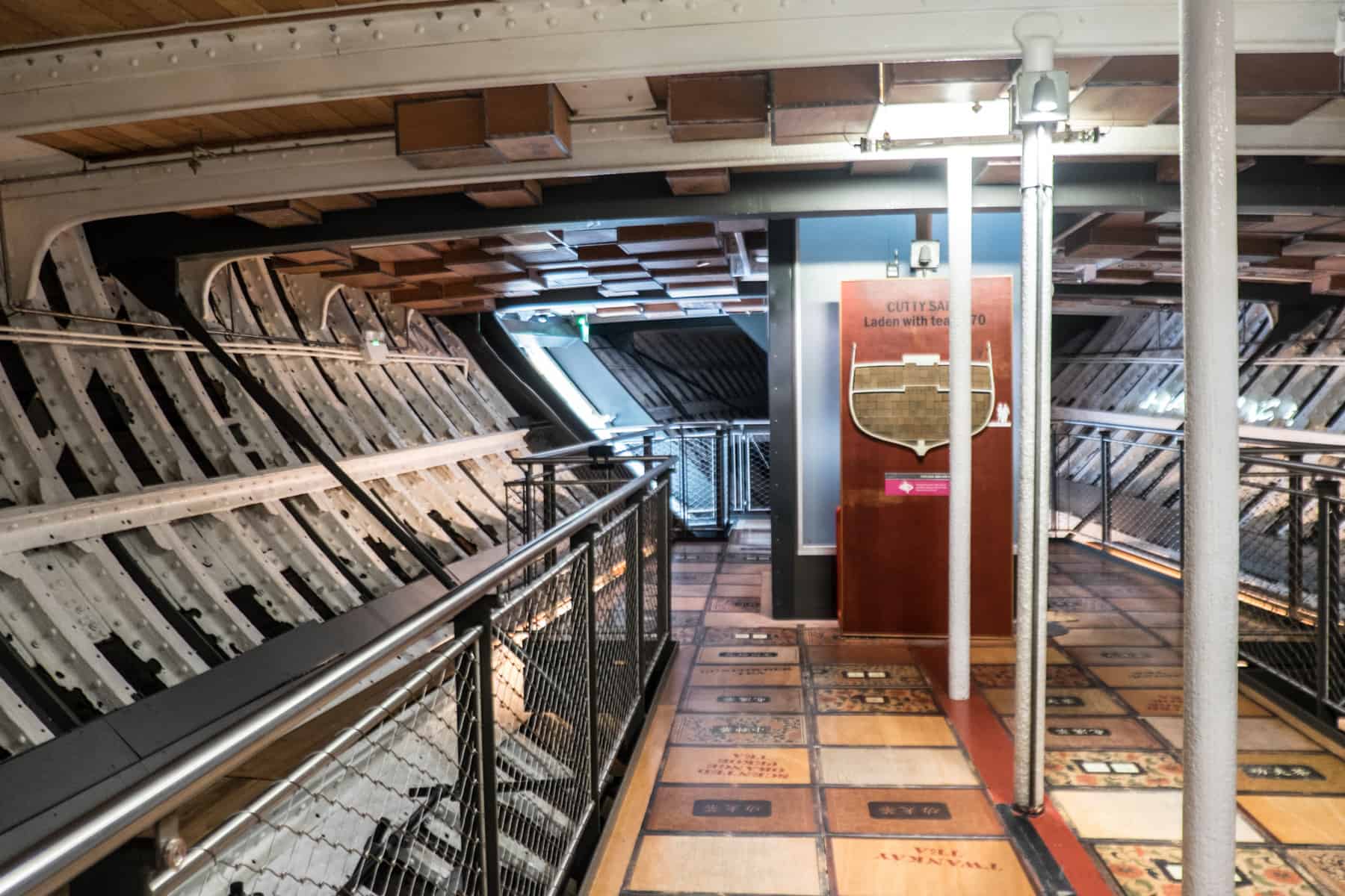 Inside the white metal and wooden lower deck of the Cutty Sark tea clipper, with tea box designed flooring and exhibition boards. 