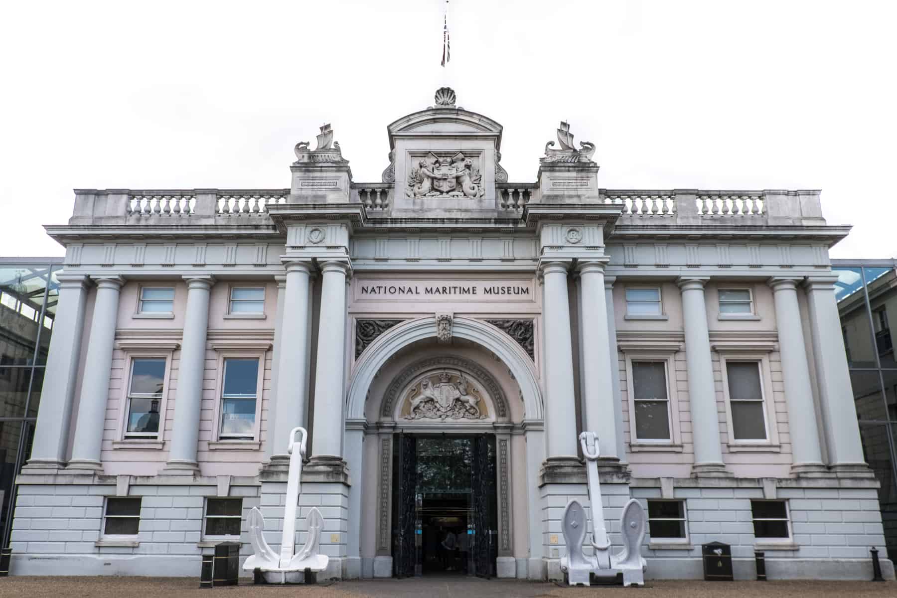 The white neo-classical facade of the National Maritime Museum in Greenwich, with large white anchors outside the front door. 