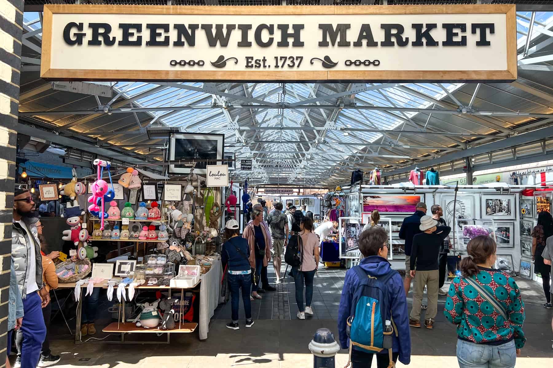 People gather around stalls selling artwork under a sign which reads: Greenwich Market Est.1737.