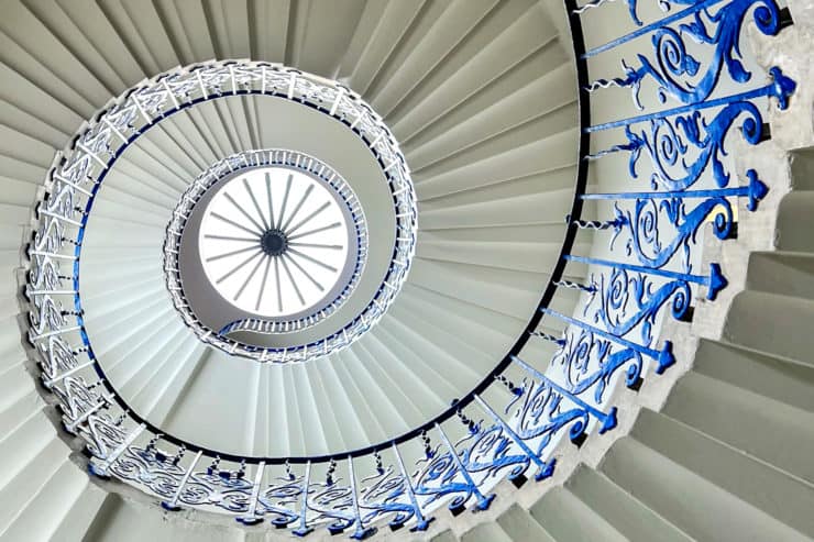 A view looking up a spiral white staircase with electric blue metal banisters - the Tulip Stairs in Greenwich.