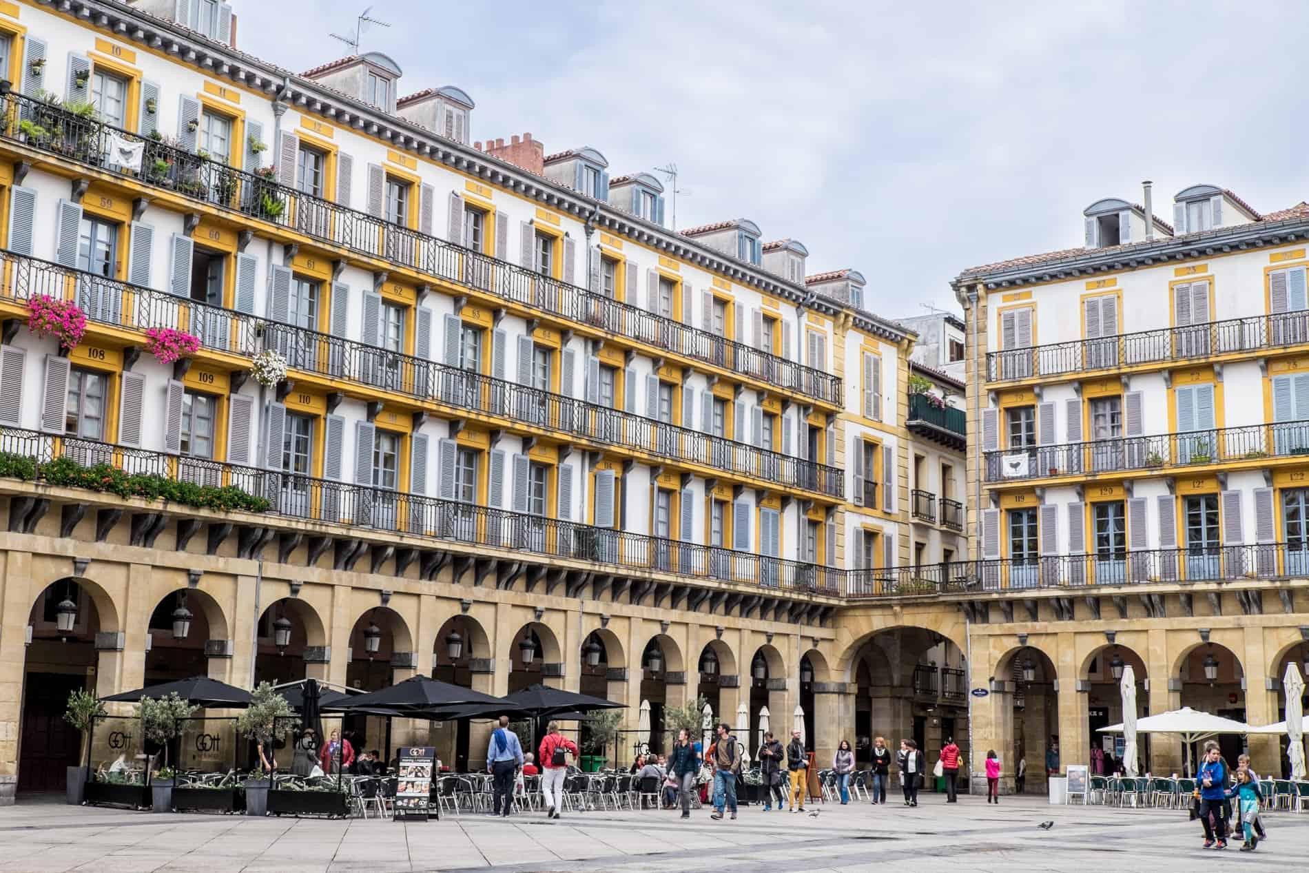 A large building on Constitution Square in San Sebastian with a four story building lined with yellow window frames. 