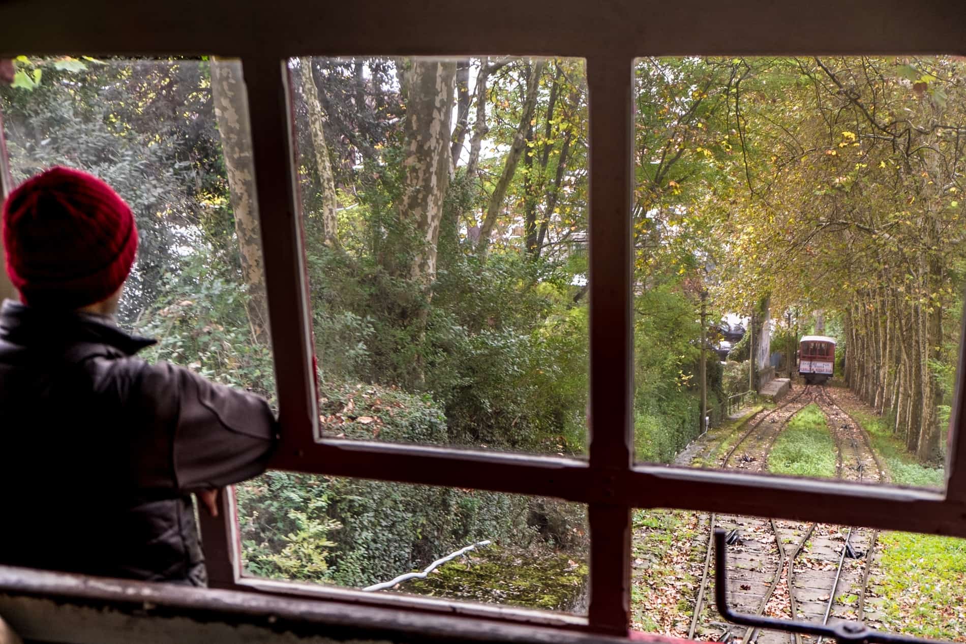 A man in a red hat looks out of the funicular car window as it travels up the green hill of Mount Igueldo in San Sebastian