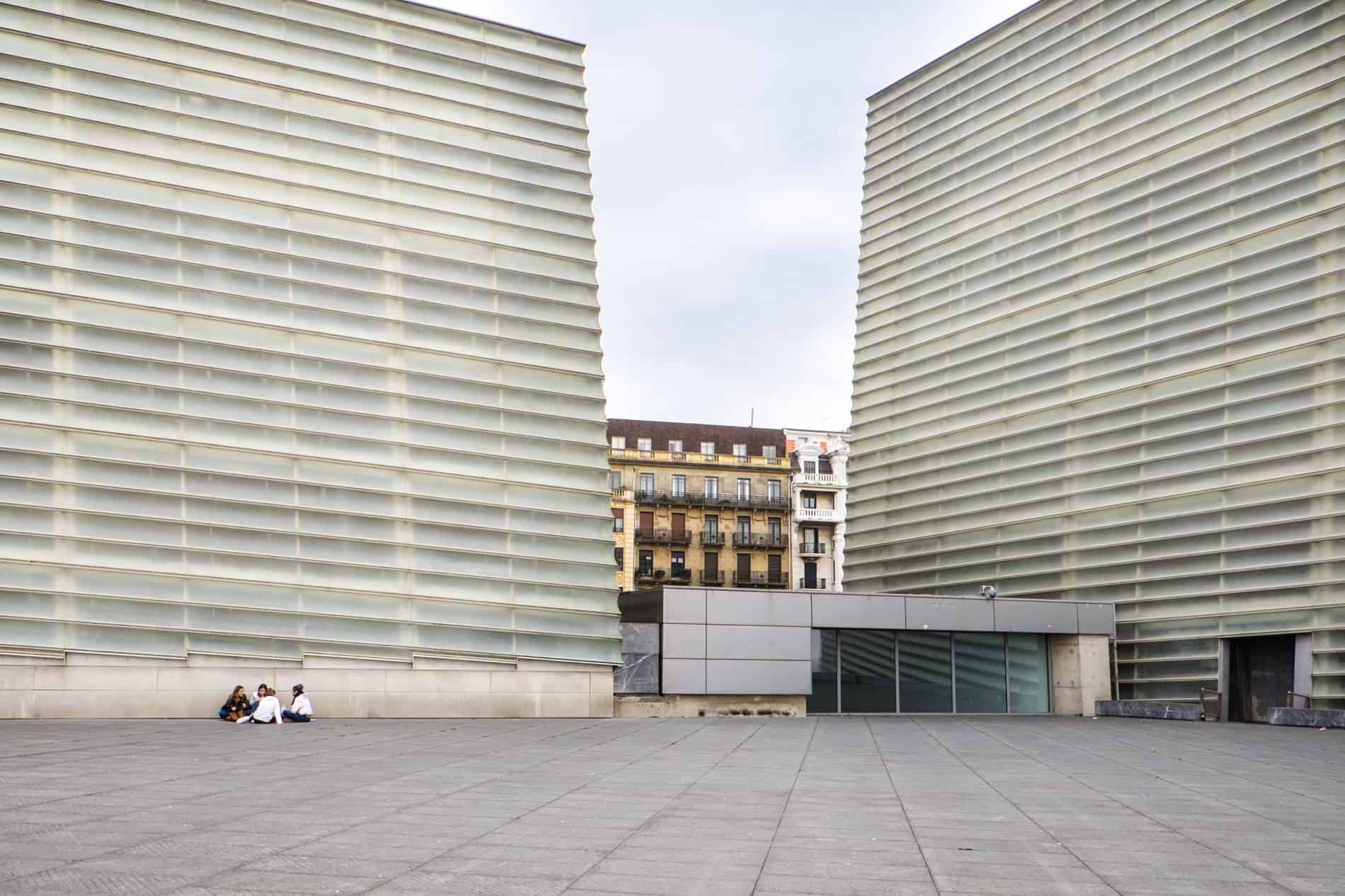 Four people sit in front of the modern, high rise walls of the Kursaal Congress Centre in San Sebastian, Spain. 