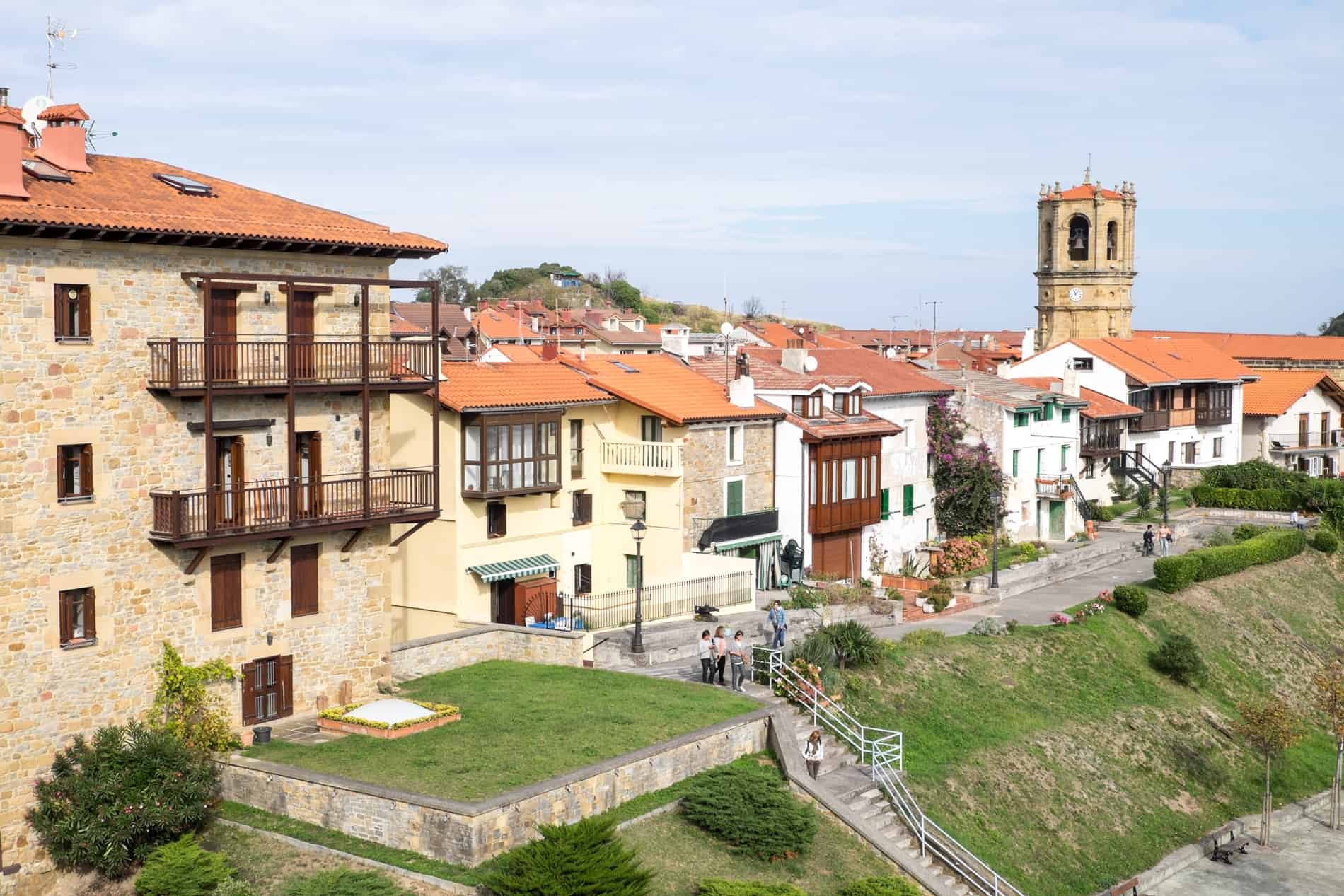 People walking along a small street lined with small earthy coloured houses in the Old Town of Getaria in Northern Spain. 