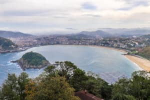 Elevated view over the coastline of San Sebastian - a city by the sea, surrounded by low-lying mountains.