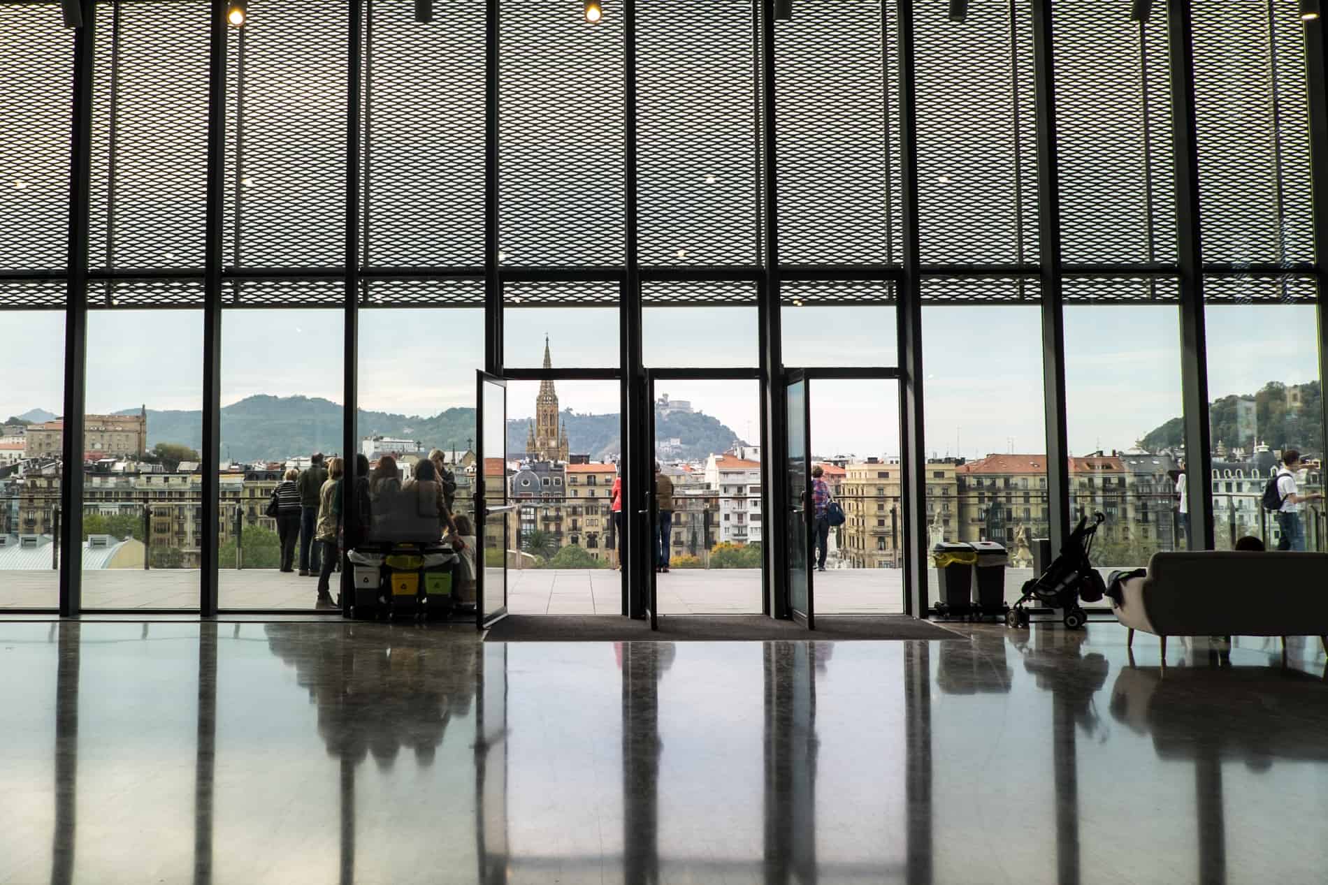 People stand at a platform outside a cultural centre looking out to a view of san Sebastian city.