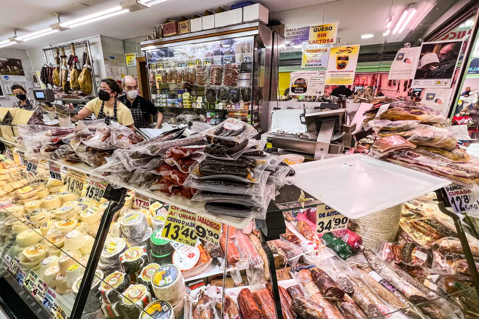 A cheese and meat stall piled high with produce, inside Mercado El Fontán in Oviedo. 