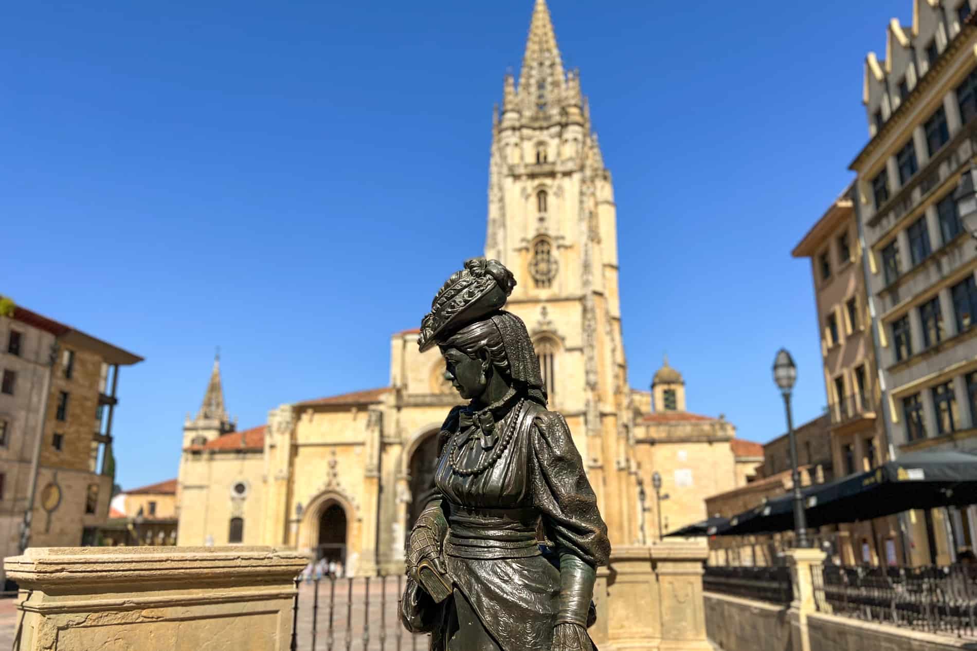 The La Regenta statue in Oviedo of a woman in elaborate dress and headpiece, standing in front of the city's cathedral.