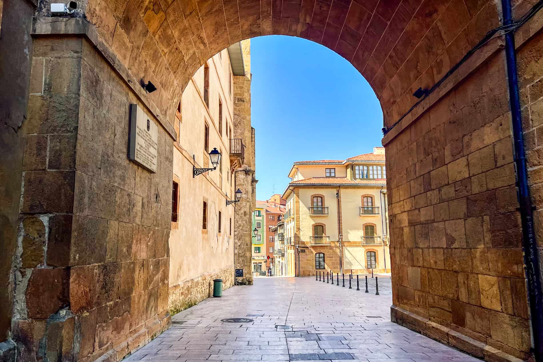 A golden brown stone archway that looks towards pastel coloured buildings. 
