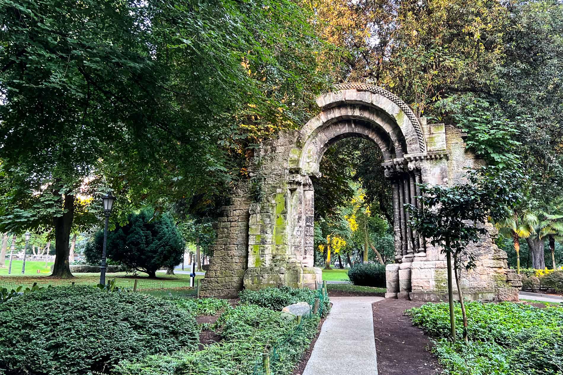 The stone archway ruins of the old San Isidoro Church in the lush green Campo de San Francisco park in Oviedo.