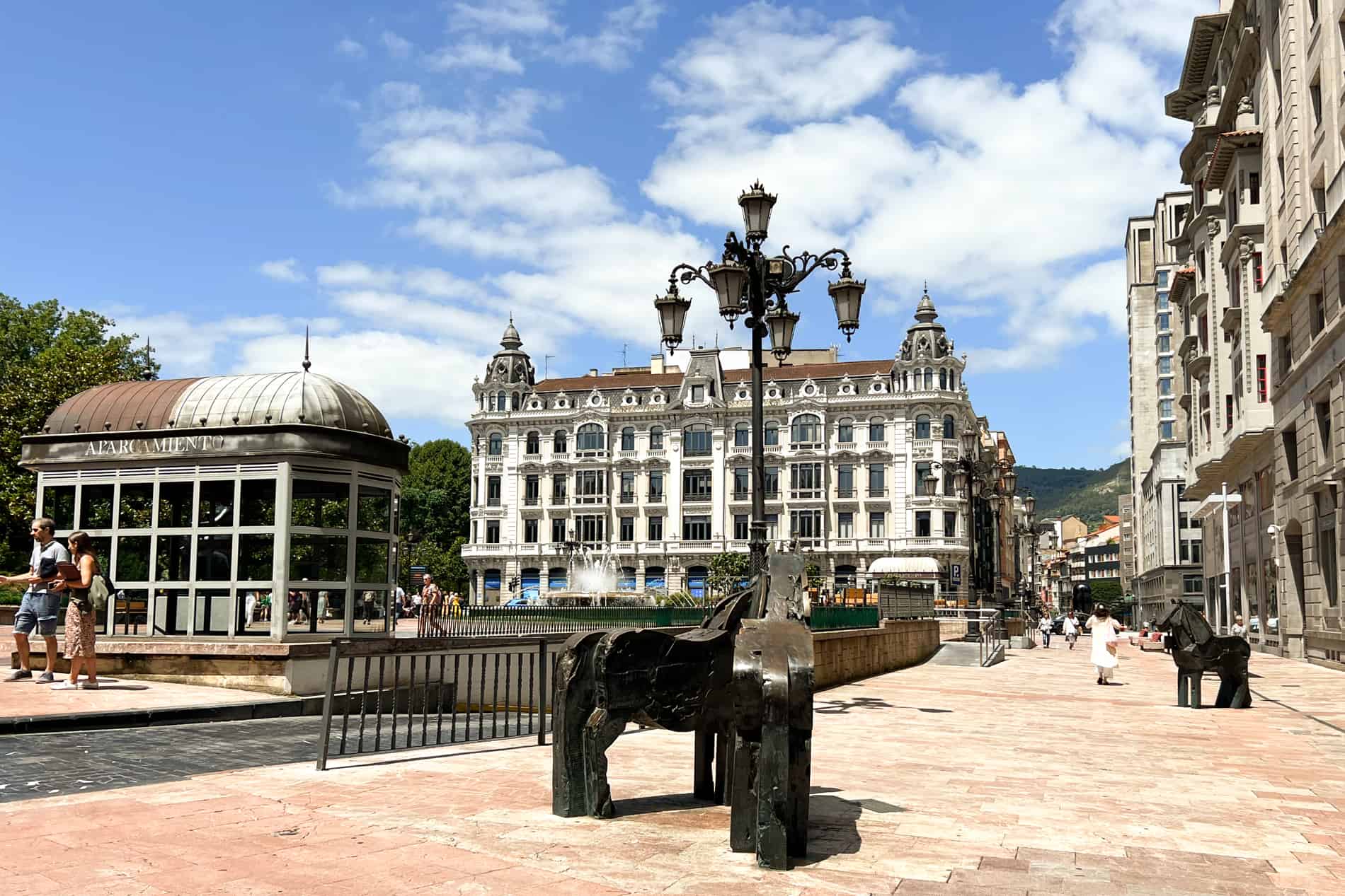 Bronze sculptures of horse on a street leading to a fountain and a grand, white building in old Oviedo, Spain. 