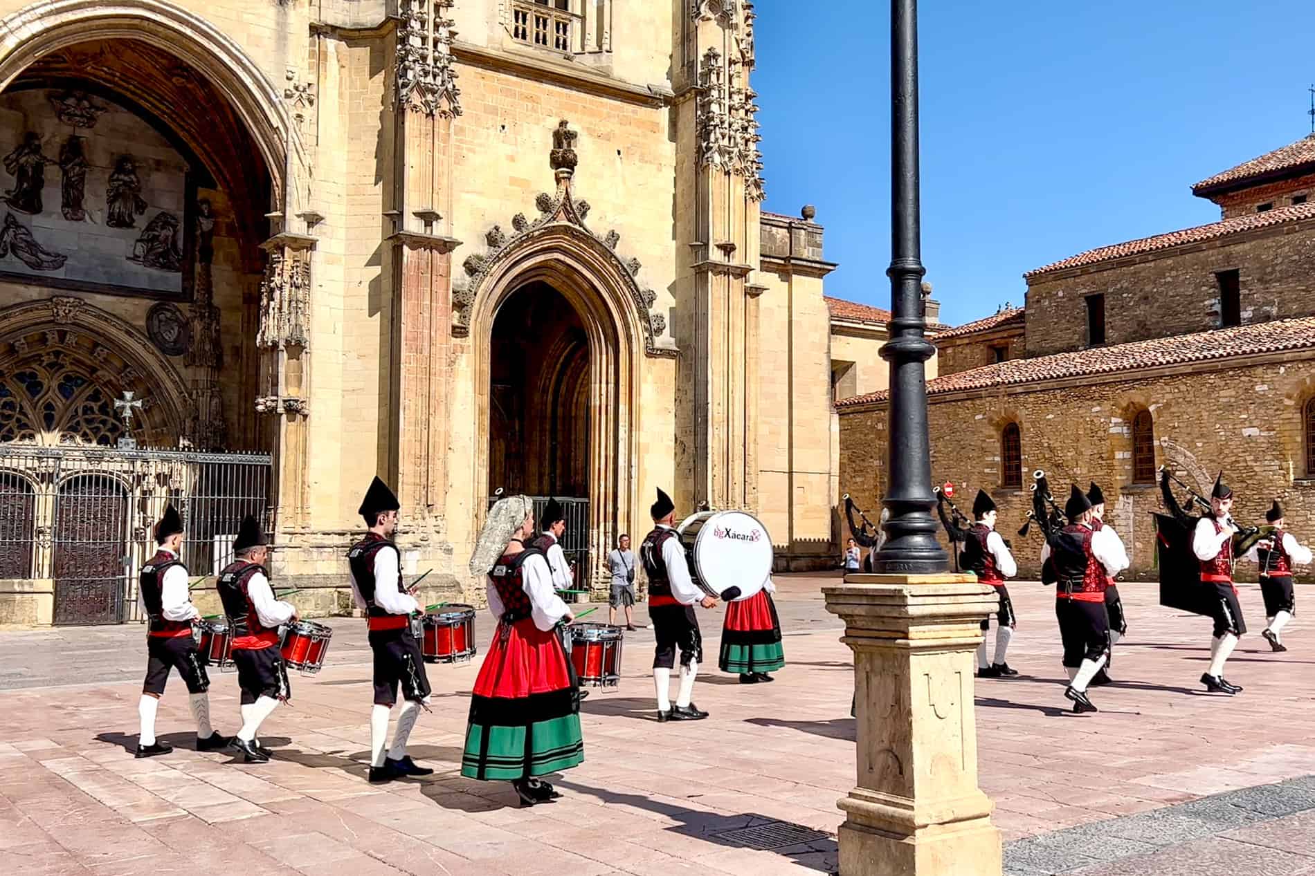 A band in black, white, red and green folk dress perform with drums and Gaita Asturiana bagpipes outside the cathedral in Oviedo, Spain.