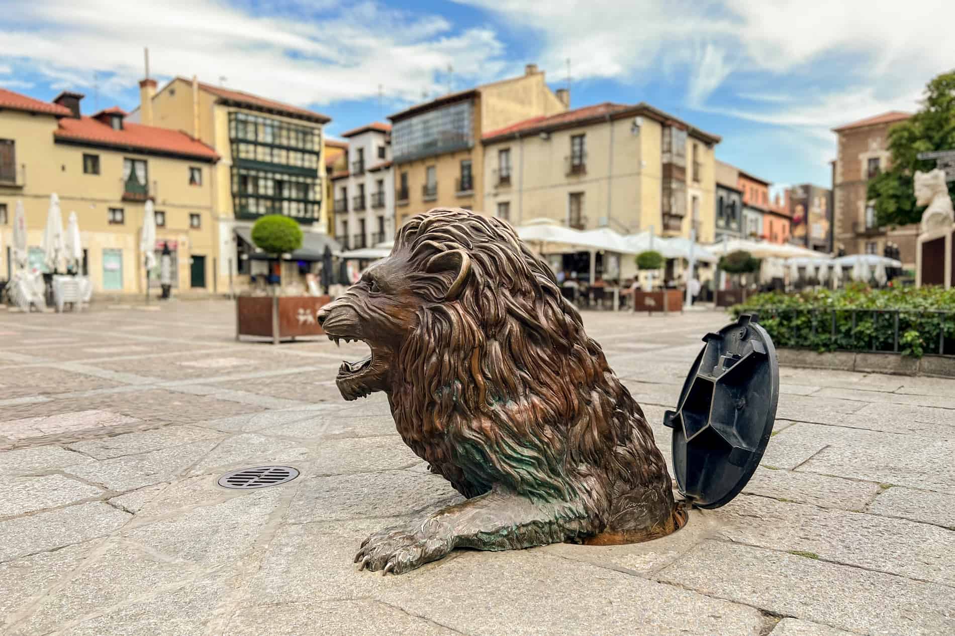 A bronze sculpture of a lion coming out of a drain hole in a public square in León city. 
